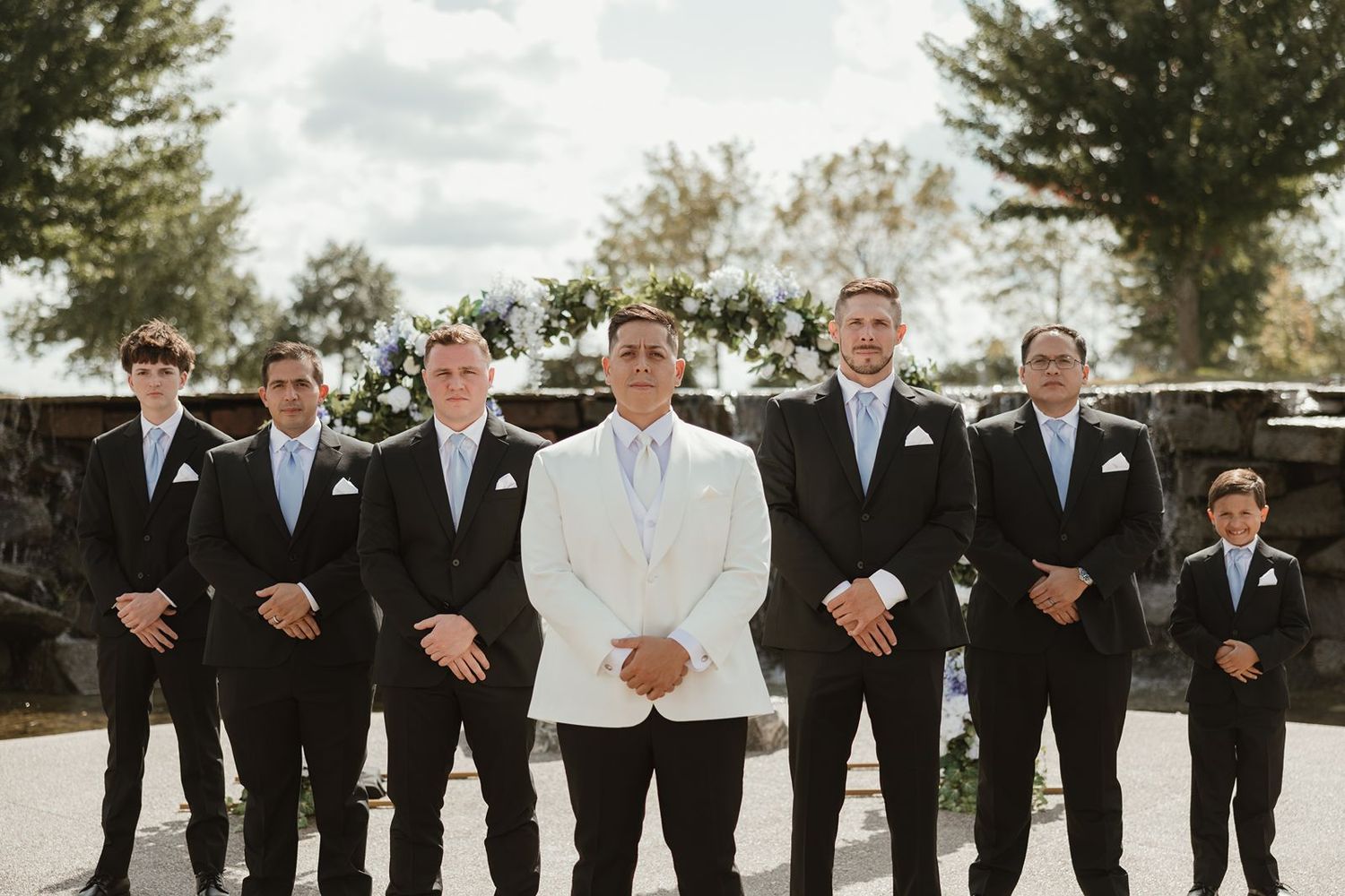 A formal wedding party portrait with groomsmen in black suits and groom in white jacket.