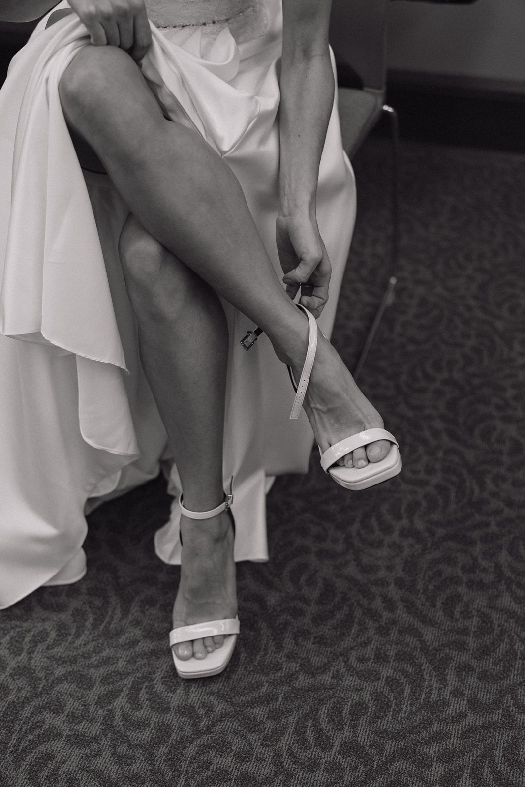 Close-up black and white shot of bride fastening white sandal strap.