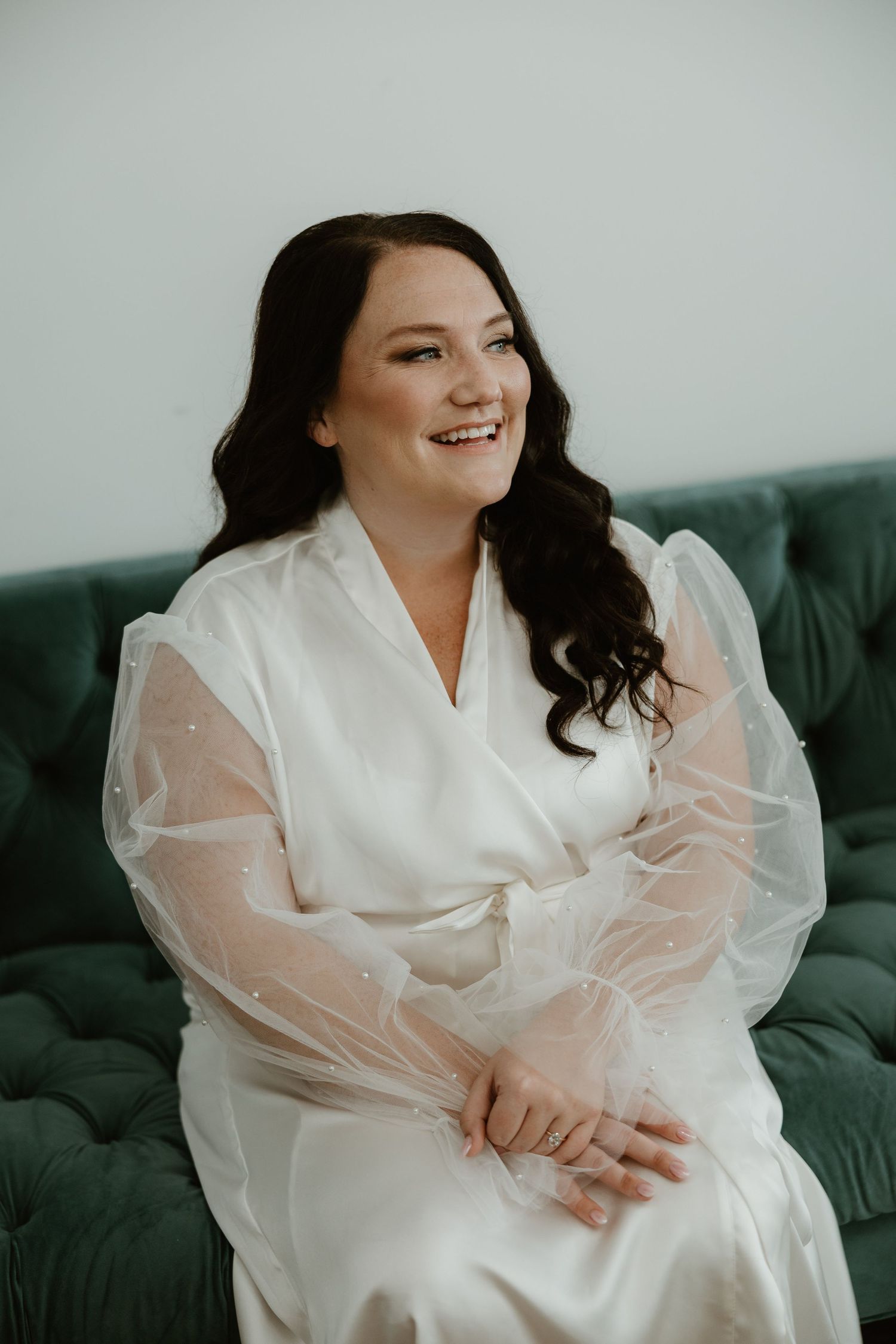 Elegant ivory sheer sleeve robe worn while sitting on emerald green tufted velvet sofa.