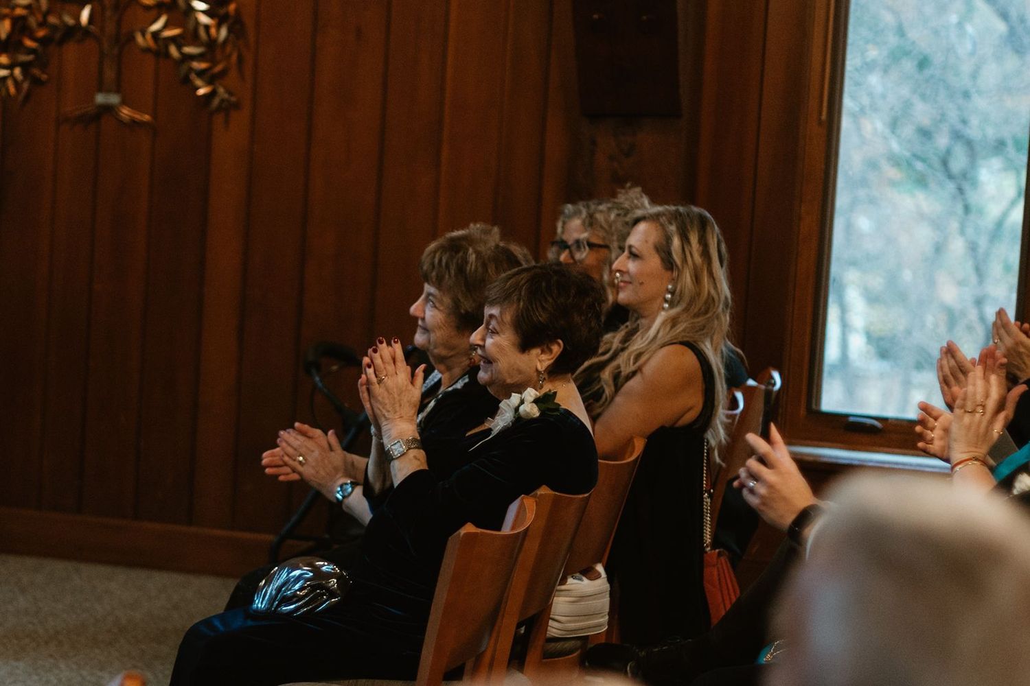 Wedding guests clapping and celebrating during ceremony in wooden chapel.