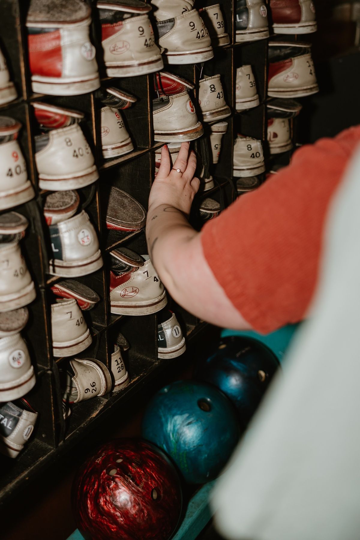 Rows of white bowling shoes on shelves with colorful bowling balls in the foreground at a bowling alley.