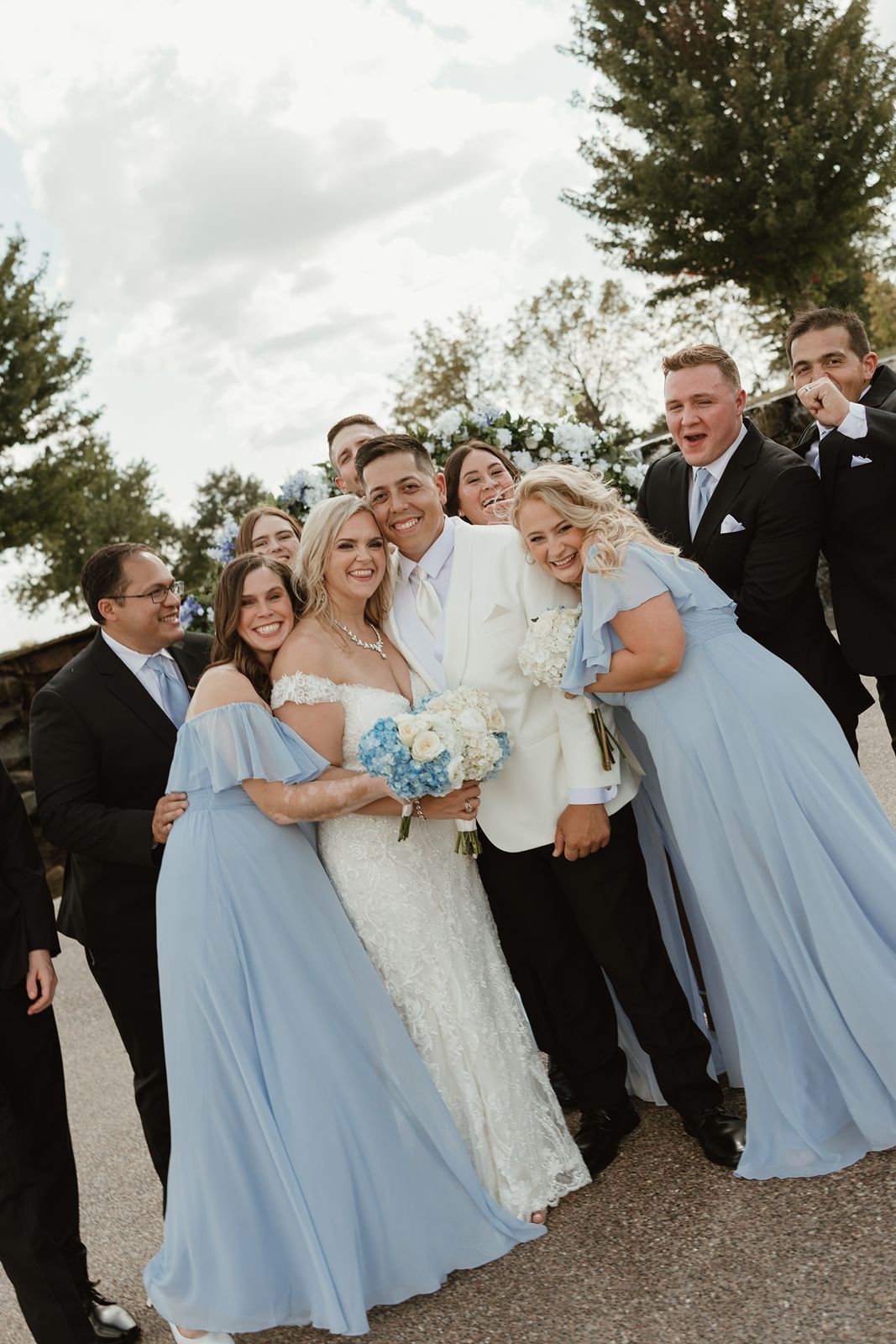 A wedding party poses together outdoors with bridesmaids in powder blue dresses.