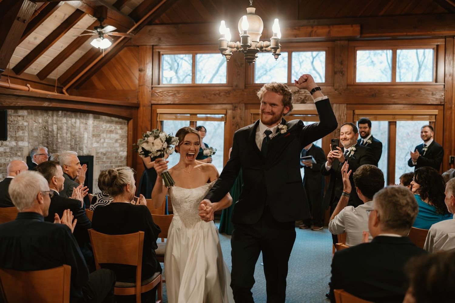 Newlyweds celebrate during their wedding ceremony in a wood-paneled room with exposed beams.