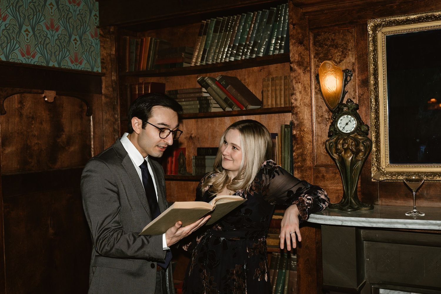 Couple exploring books together in cozy vintage library setting with warm ambient lighting.