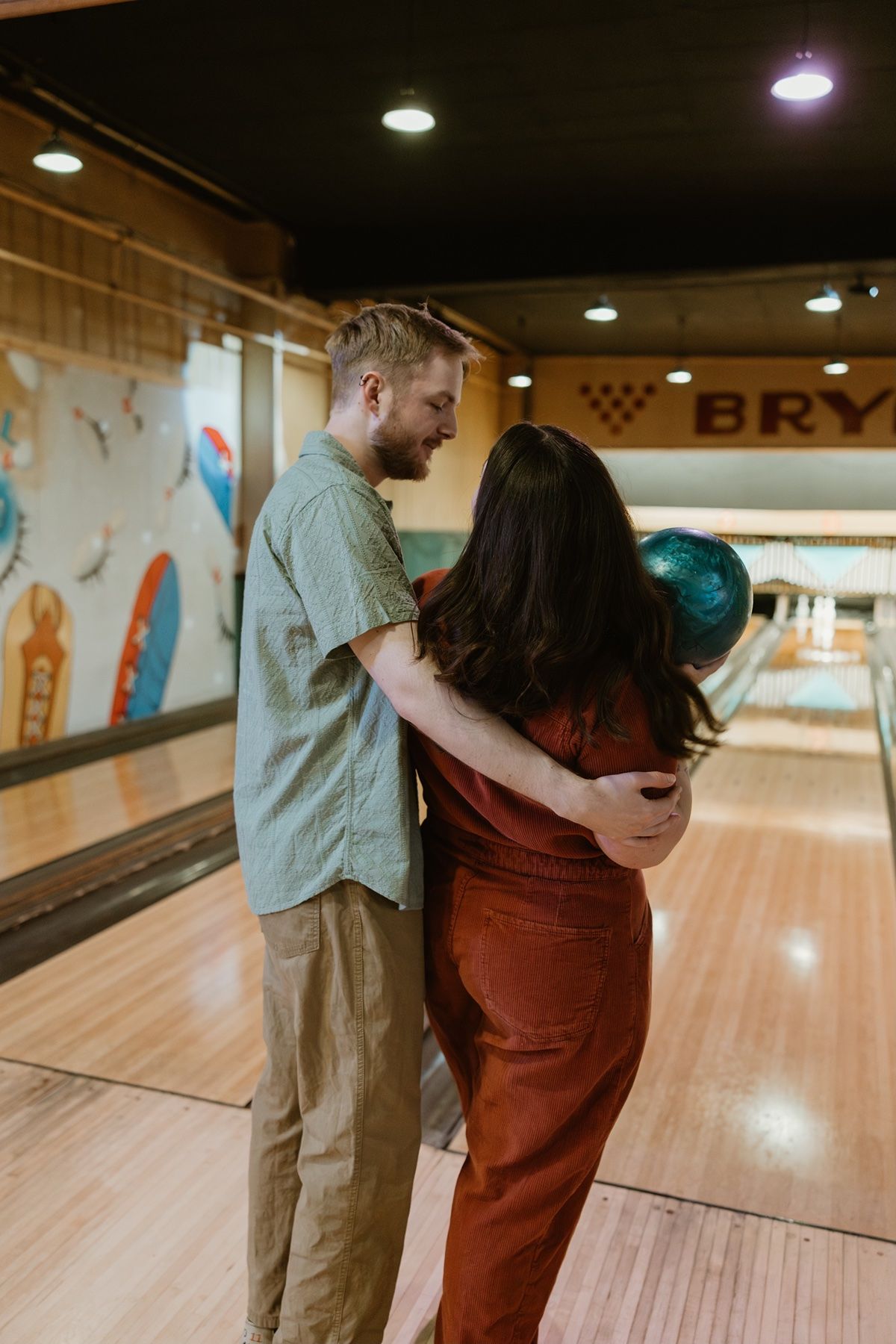 A couple embraces while bowling at a retro-style bowling alley with wooden lanes and mood lighting.