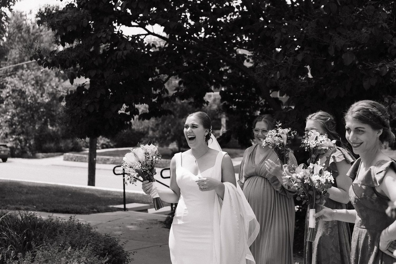 Black and white photo of wedding party celebrating outdoors with joyful expressions.