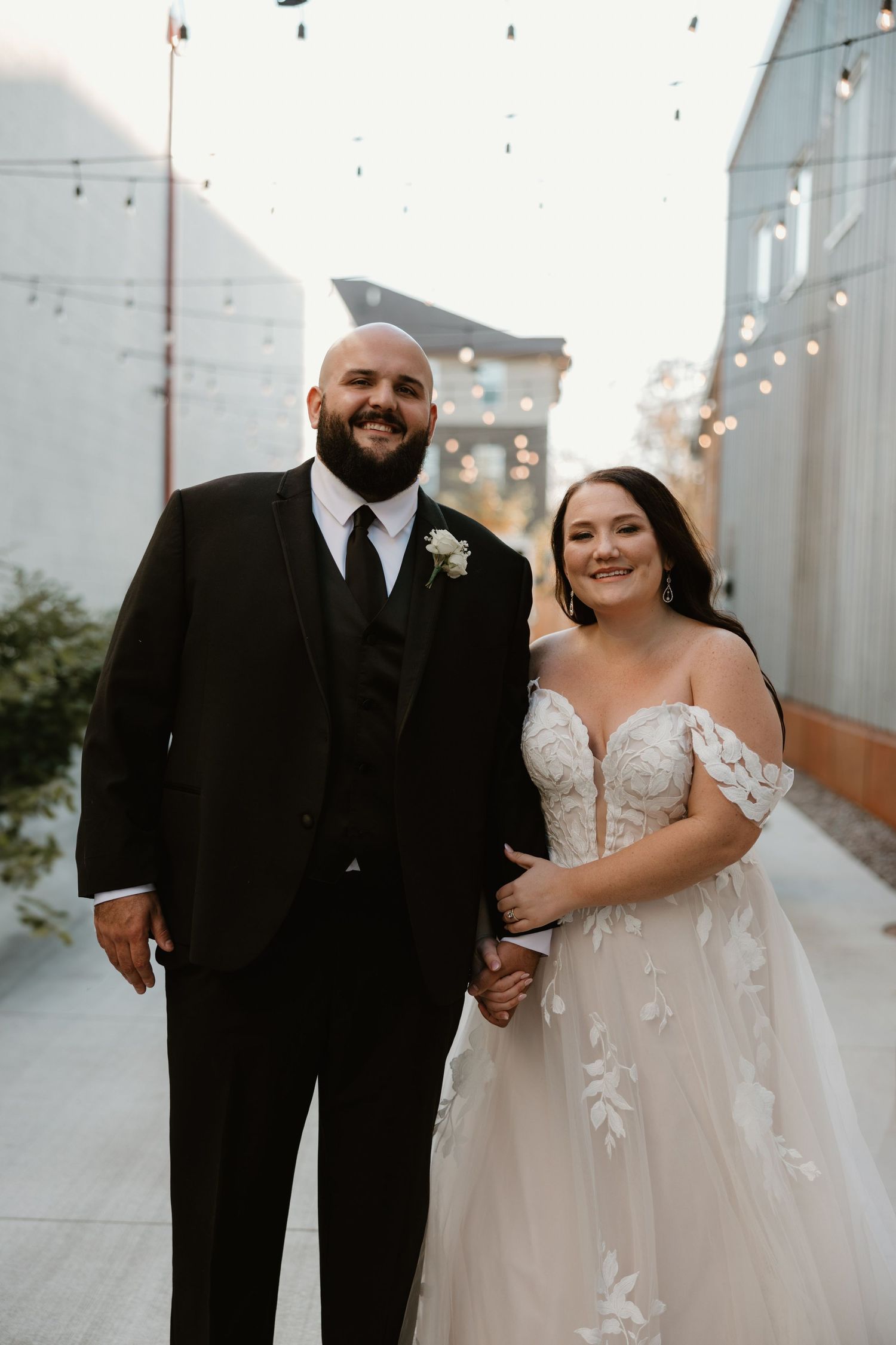 A classic bride and groom share a sweet moment outside a venue decorated with twinkling lights.