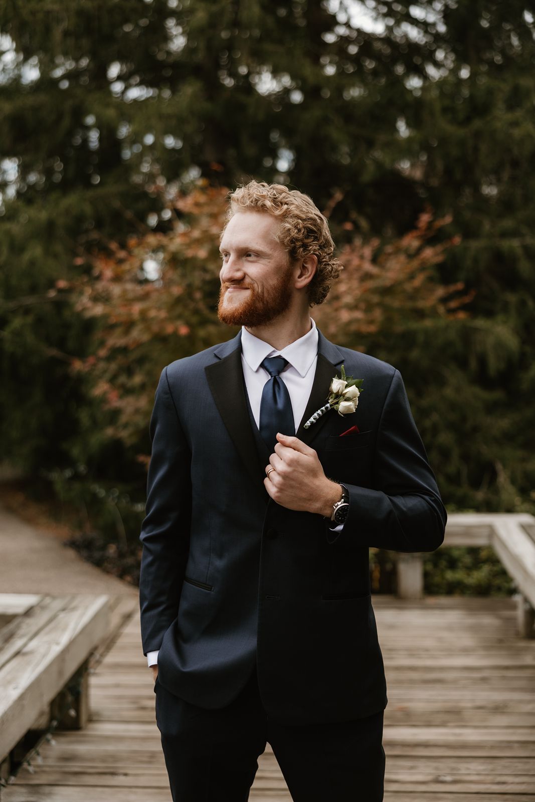 Groom in classic black tuxedo with boutonniere looking off into distance.
