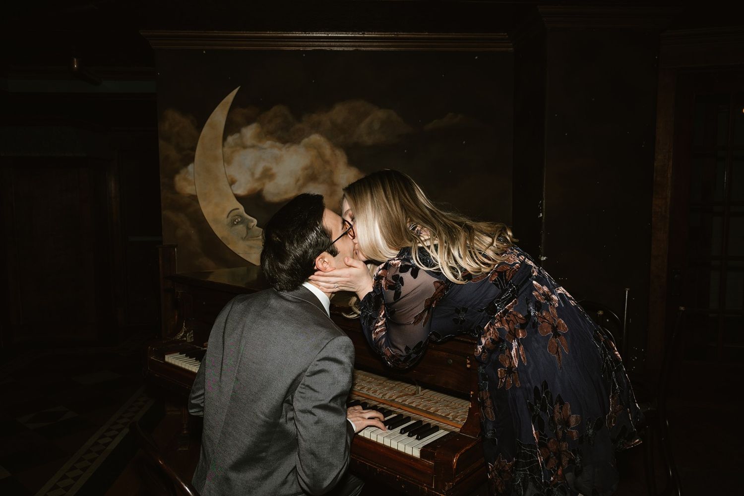 Intimate moment between a couple at a piano with a decorative moon backdrop in moody lighting.
