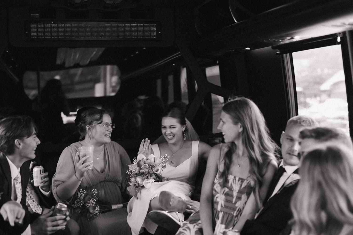 A group of people laugh together while riding in the back of a limousine in black and white photography.