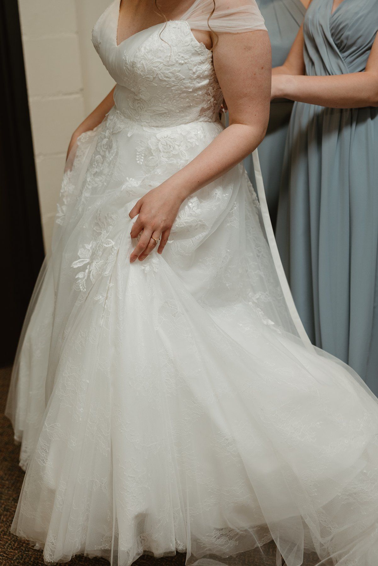 Flowing tulle wedding dress with lace bodice shown from waist down against light colored backdrop.