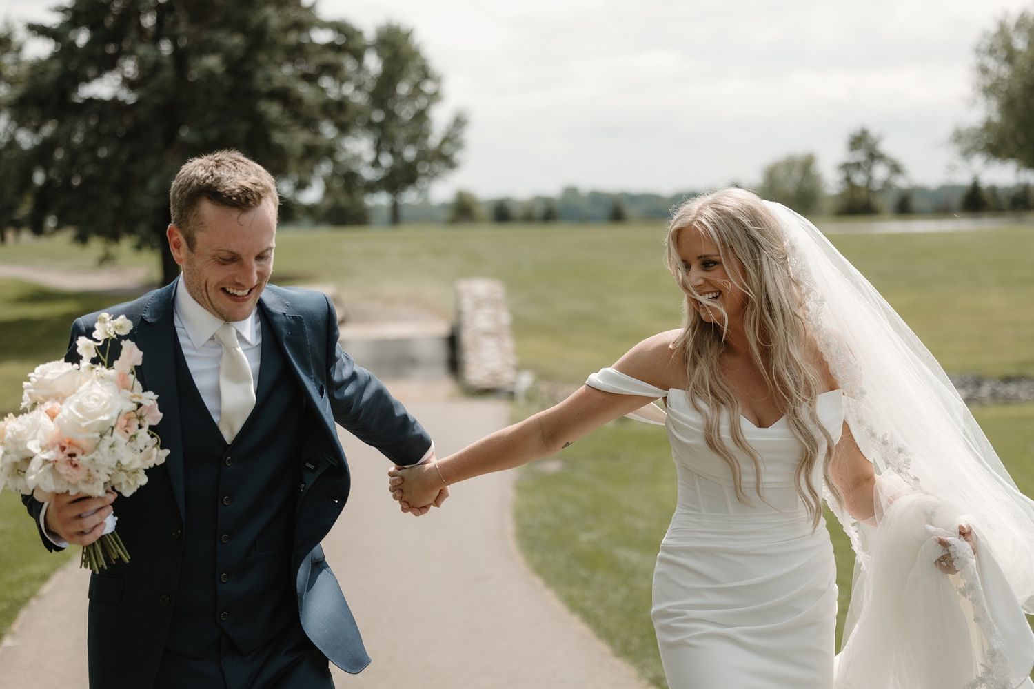 Happy bride and groom holding hands and walking outdoors on their wedding day, bride wearing white gown and veil.