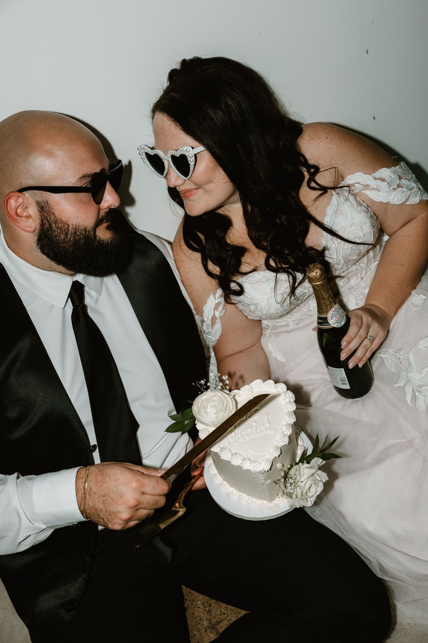 A couple in wedding attire sharing a playful moment while cutting their cake together.