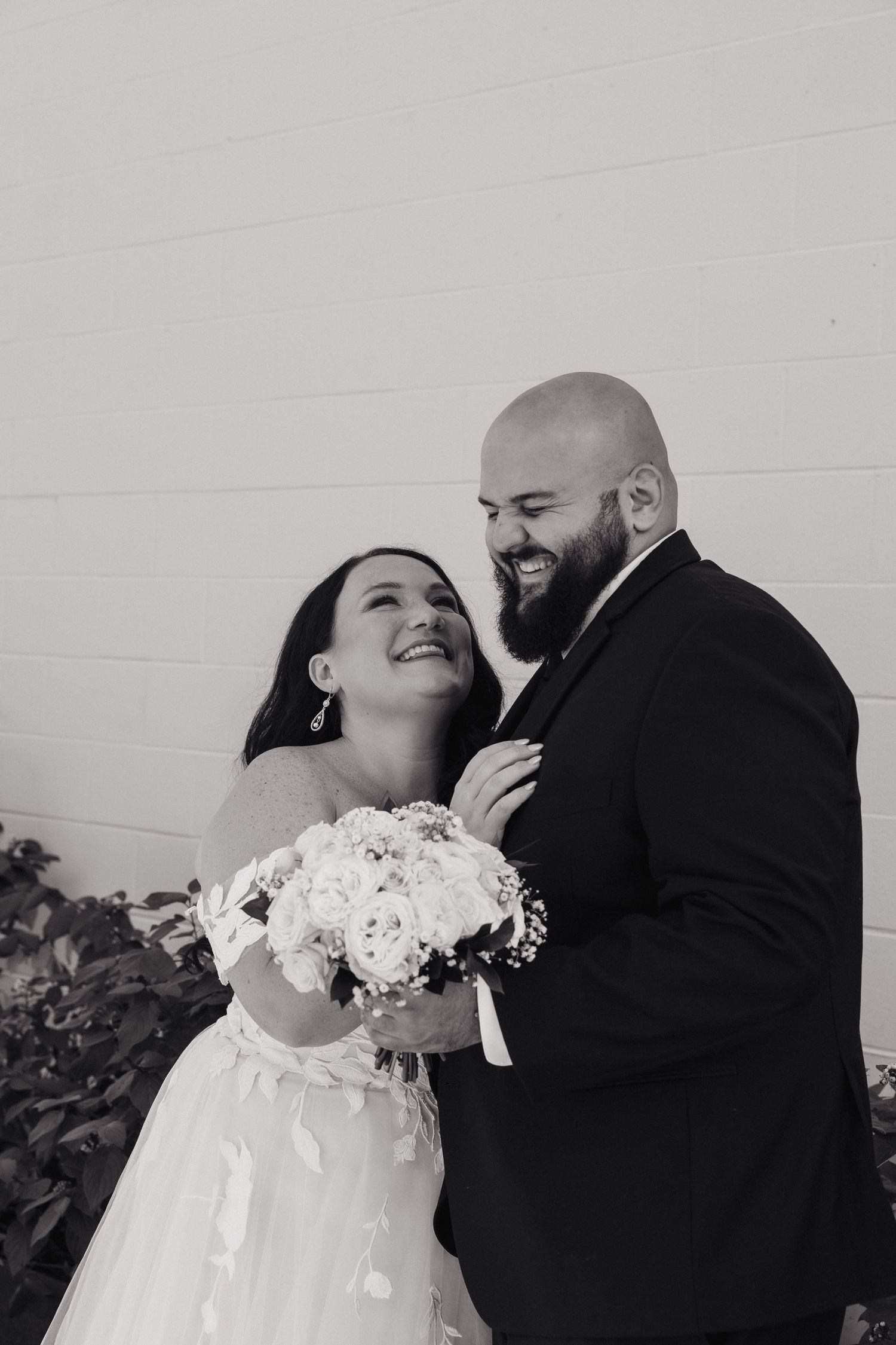 A happy couple shares a joyful moment together on their wedding day, with the bride holding a white floral bouquet.