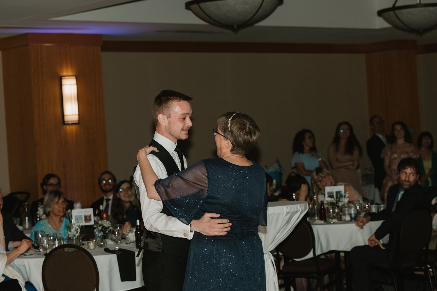 Guests dancing and mingling at an indoor wedding reception venue with warm lighting and table settings.