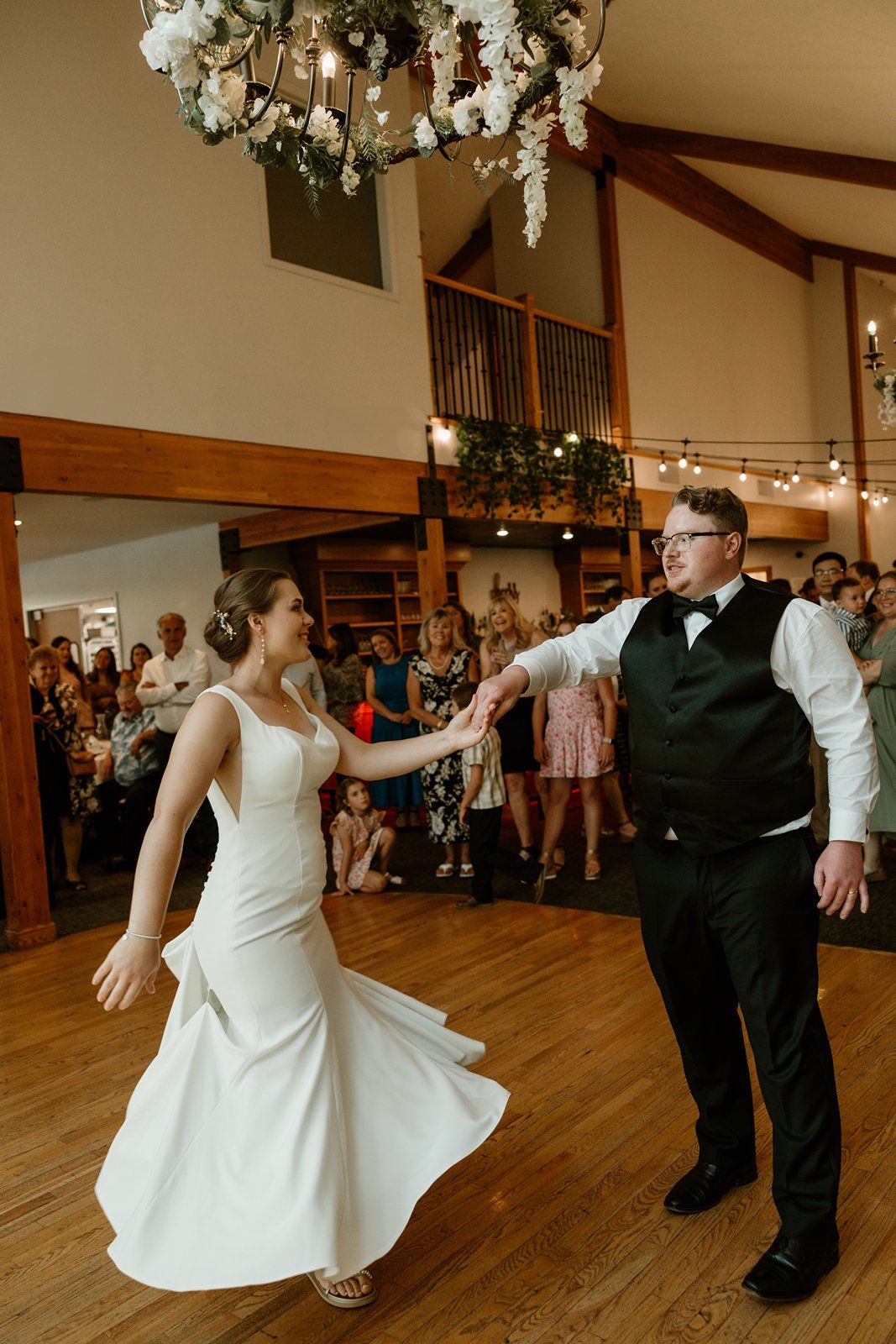 Couple dances together at a wedding reception in a rustic venue with wooden floors and exposed beams.