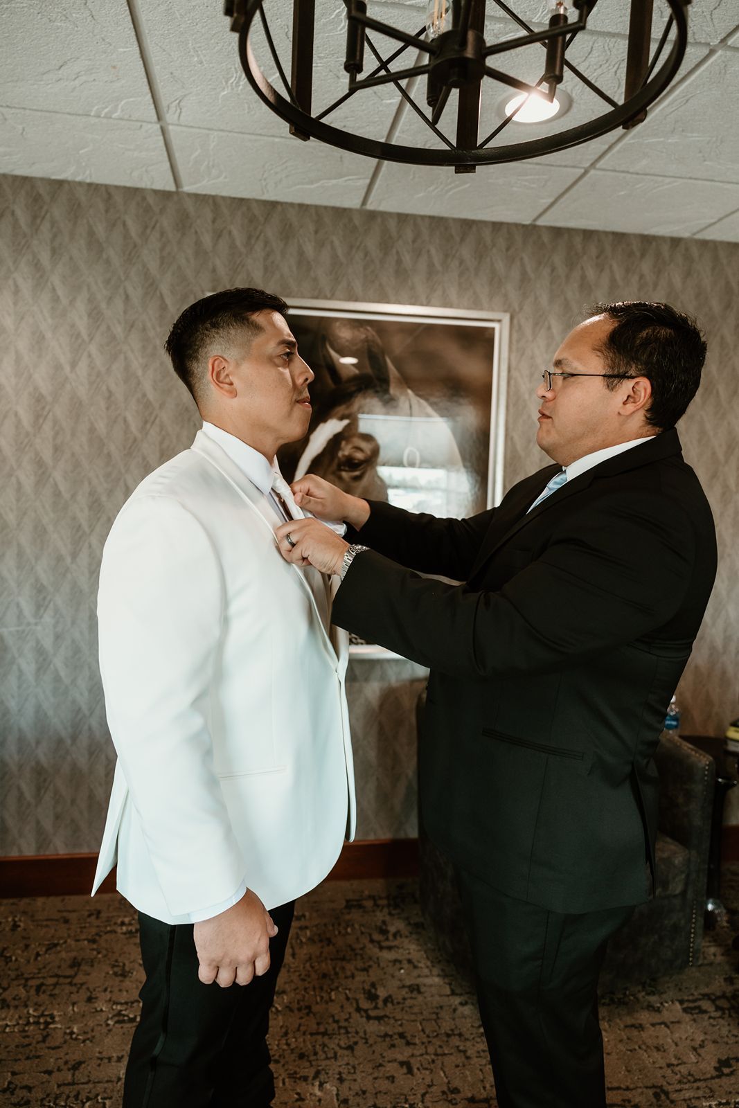 A groomsman helps adjust another's tie while getting ready for the wedding ceremony.