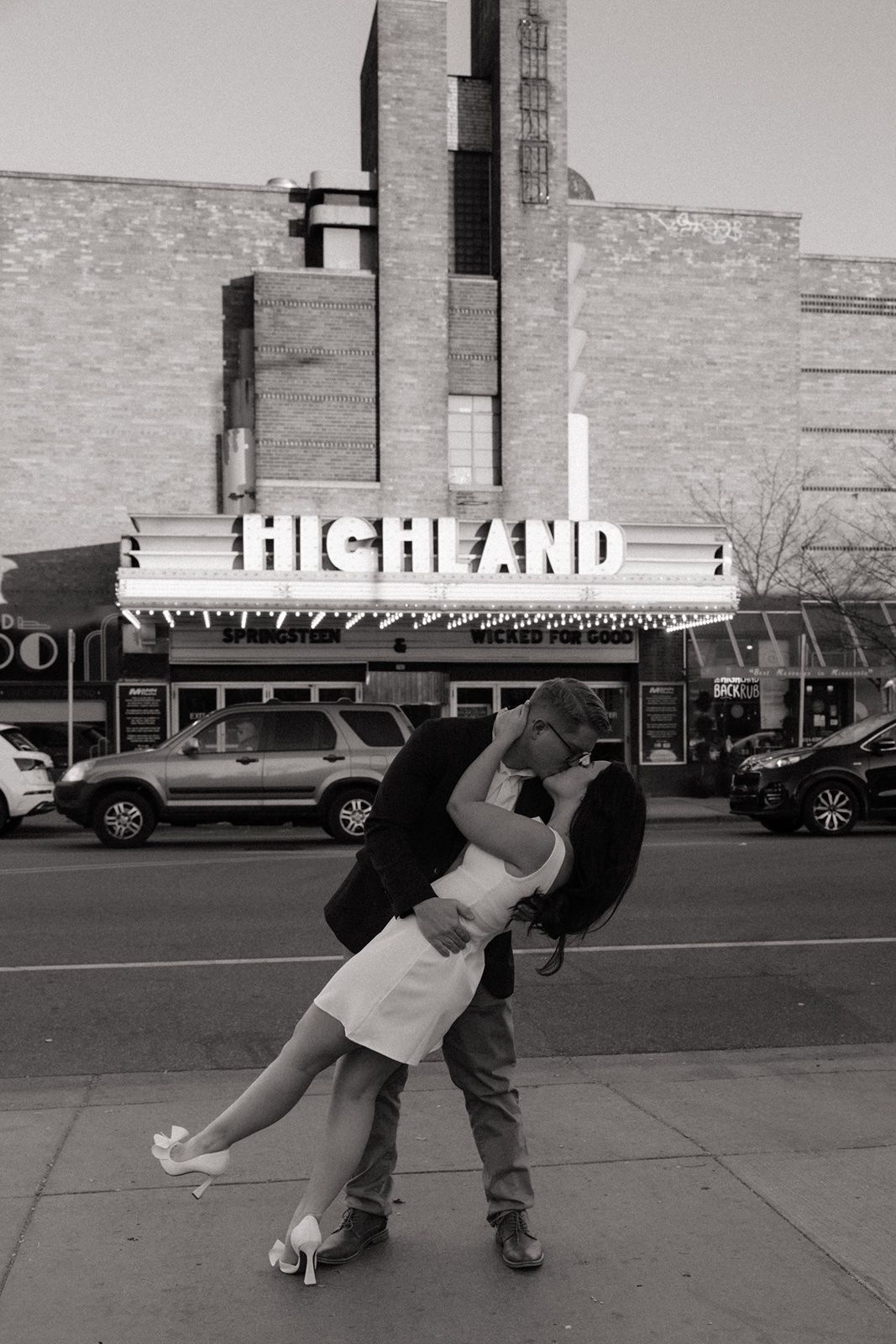 Couple sharing a romantic kiss in front of the Highland Theater marquee sign in black and white photo.