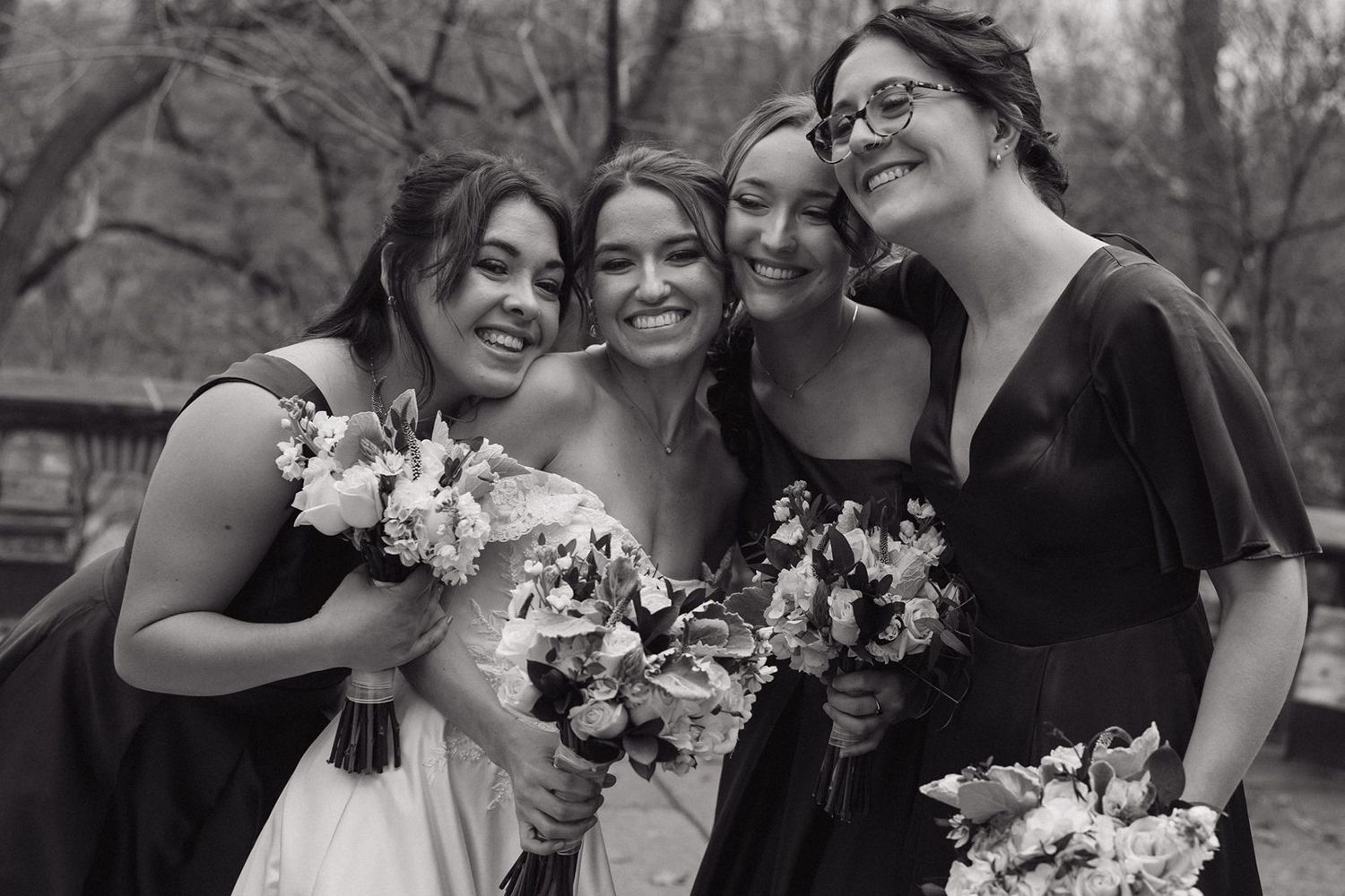 Bridesmaids holding white bouquets share a joyful moment in black and white photography.