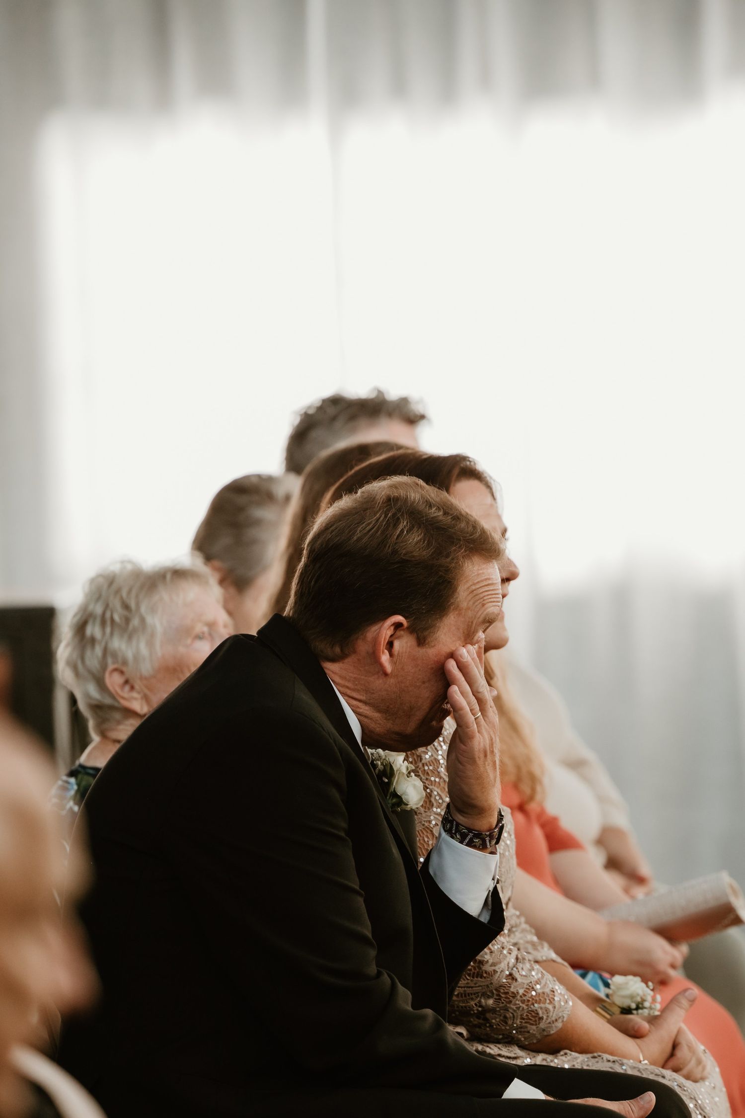 A guest seated during a formal event rests his hand on his face in a contemplative gesture.