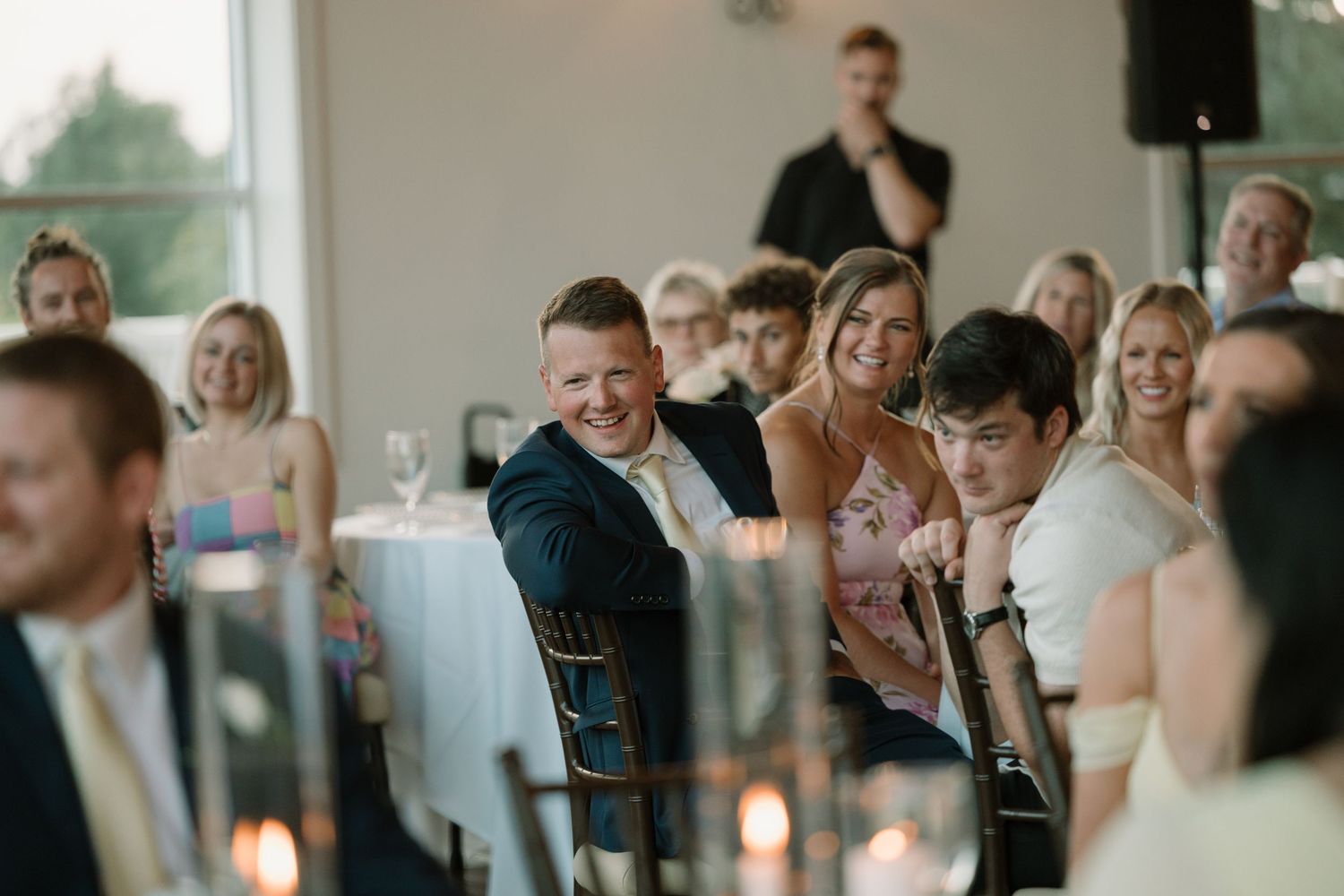 Wedding reception guests seated at tables in an indoor venue with warm lighting.