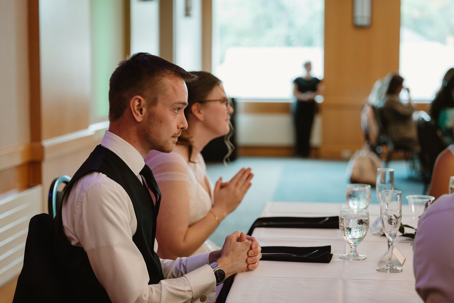 Wedding guests seated at reception table during an indoor celebration event.