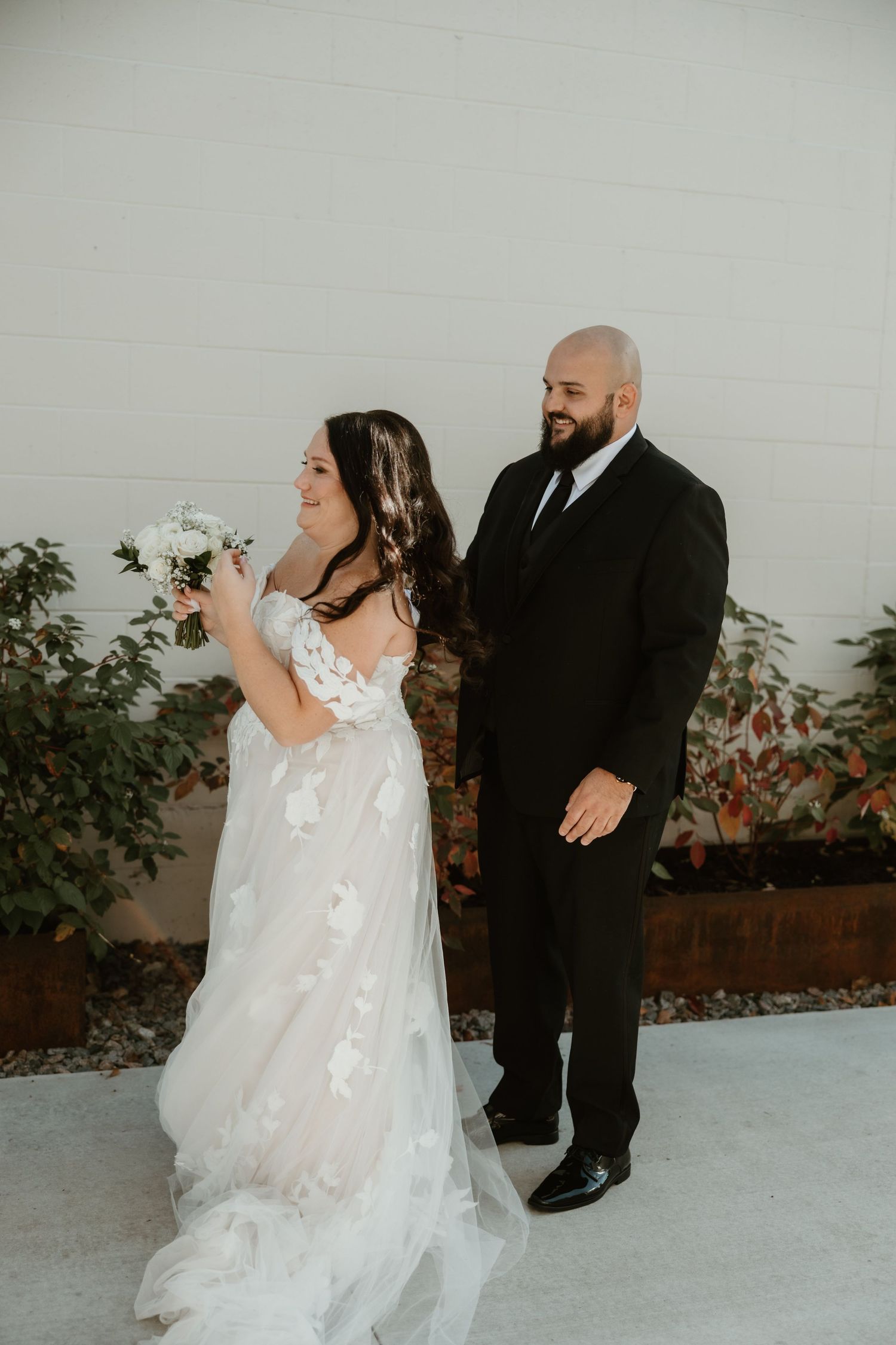 A couple shares a candid moment at their wedding, with the bride in a flowing white dress and groom in classic black suit.