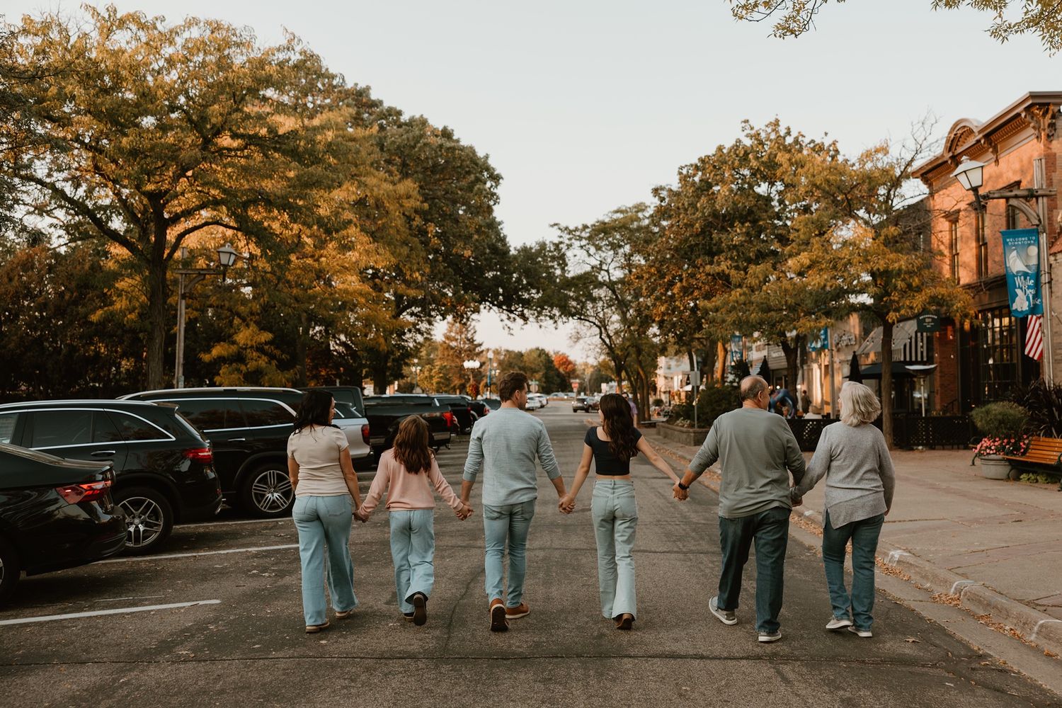 Group of family members walking hand-in-hand down a tree-lined street in a charming small town during autumn.