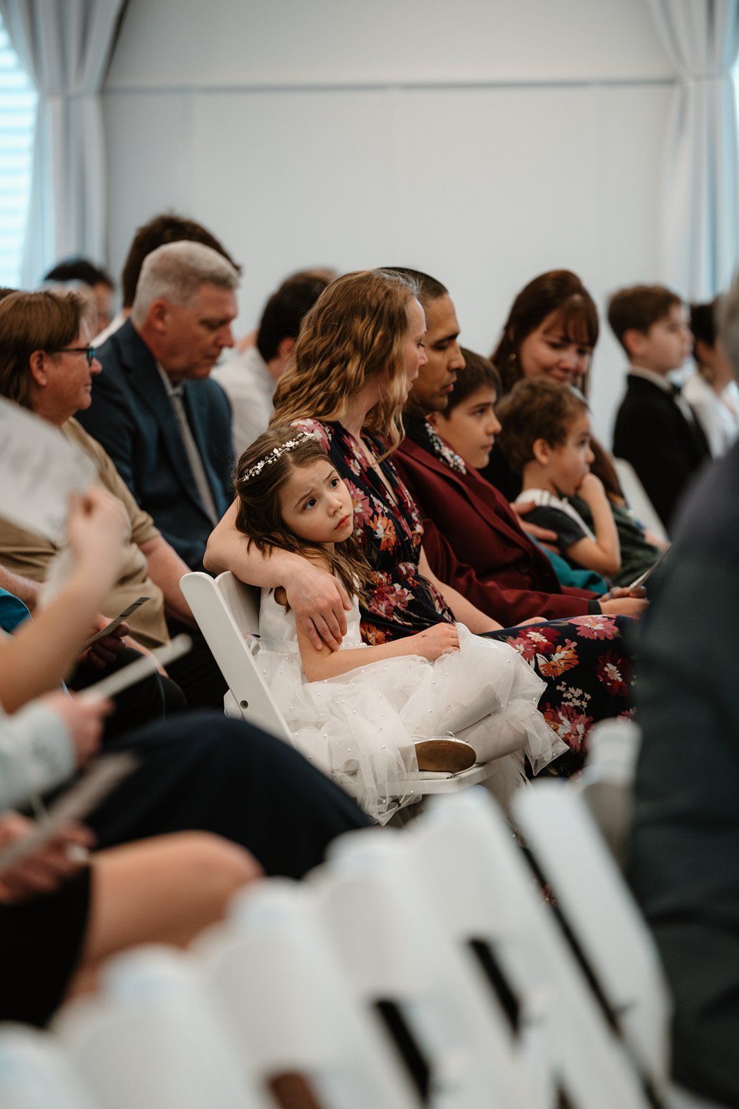 Audience members sit attentively in rows of white chairs during an indoor event.