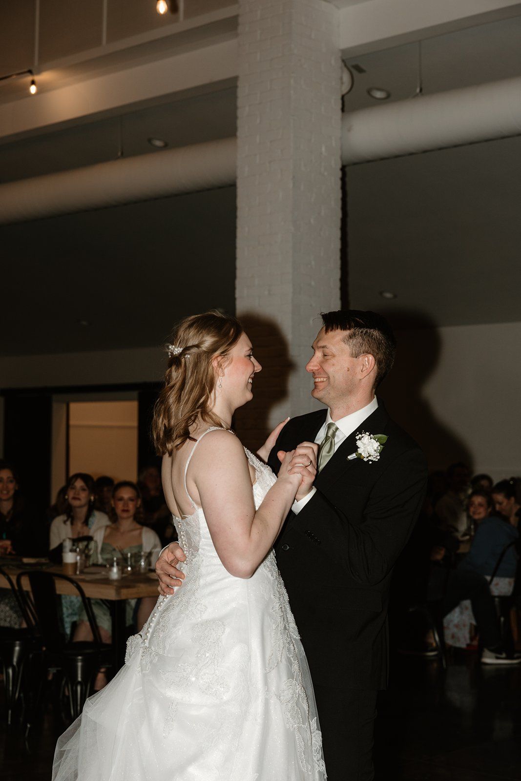 A couple shares their first dance at a wedding reception in a dimly lit venue.
