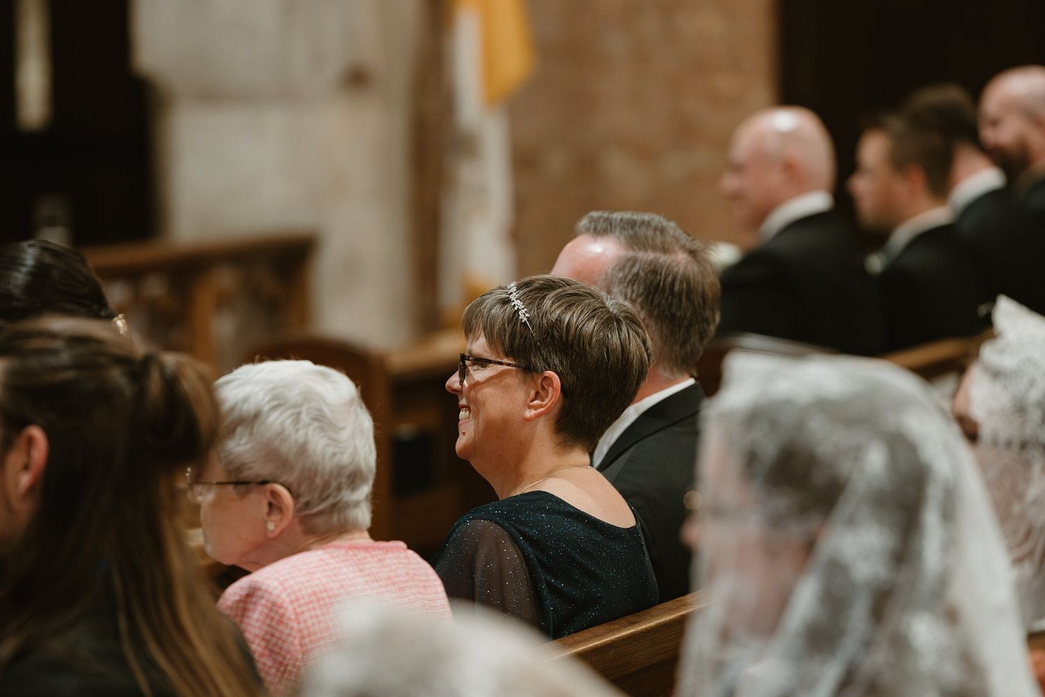 Wedding guests are seated in wooden church pews during an elegant ceremony service.