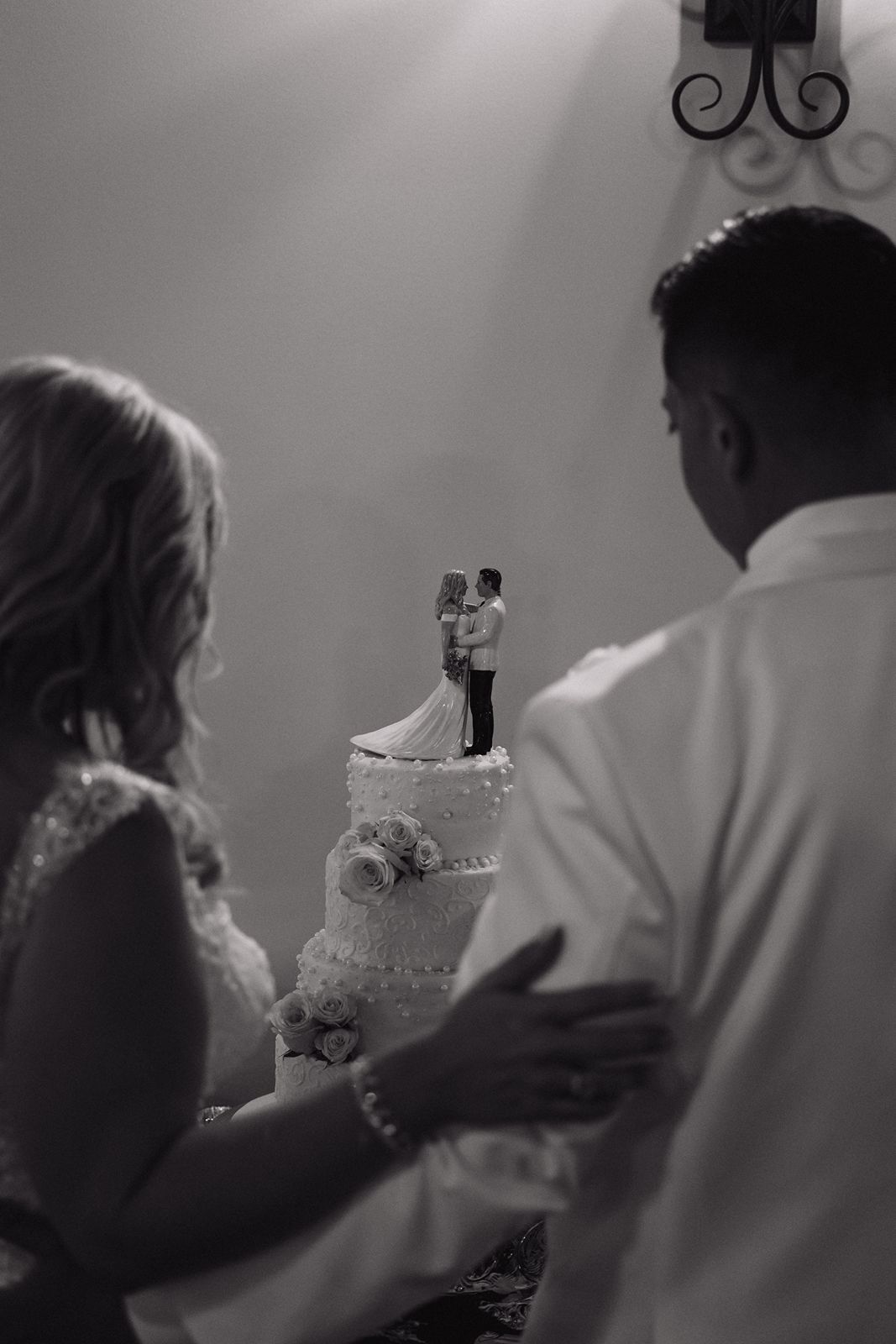 A couple admires their elegant white wedding cake topped with a traditional bride and groom figurine.