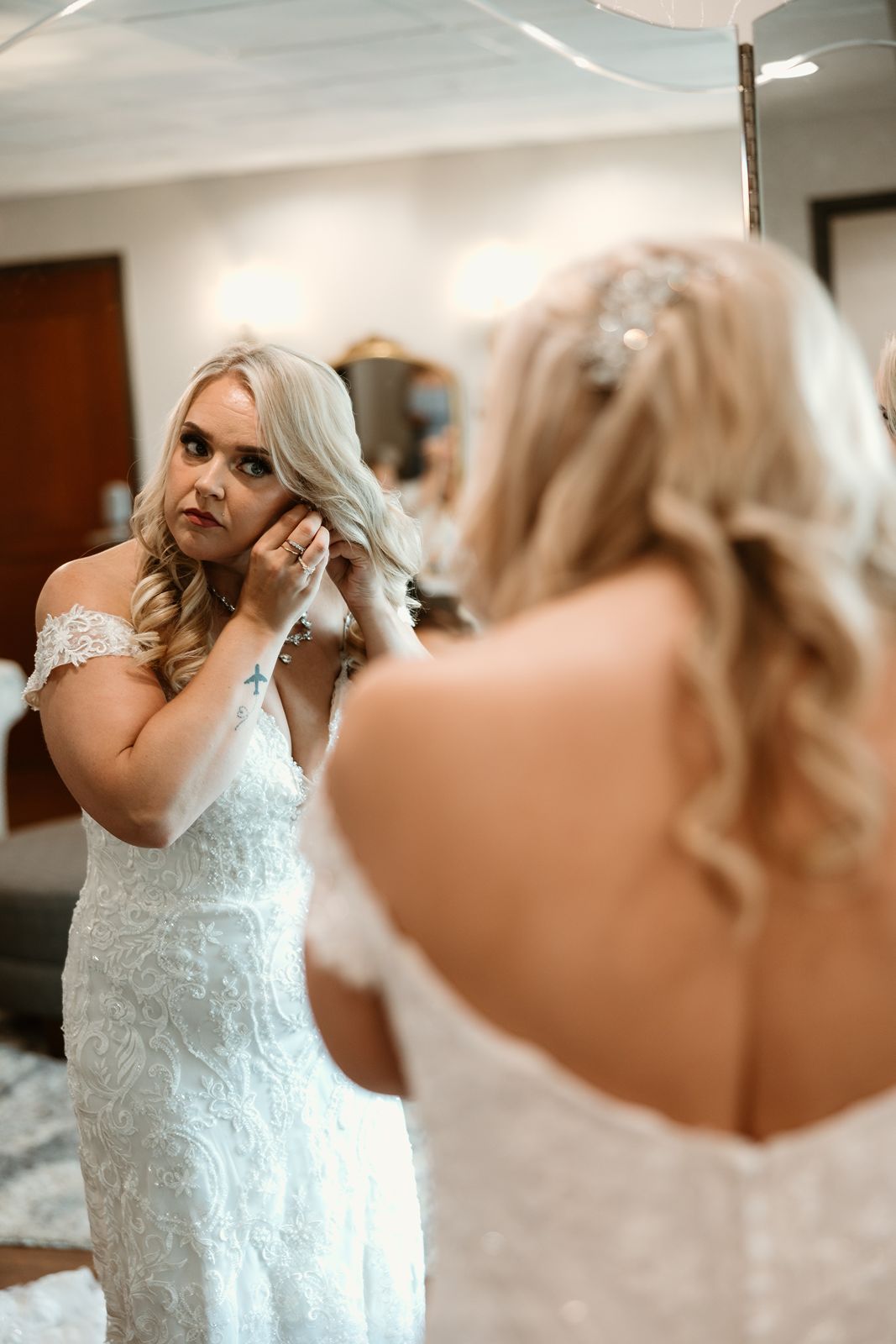 A bride adjusts her earring while looking in the mirror before the ceremony.