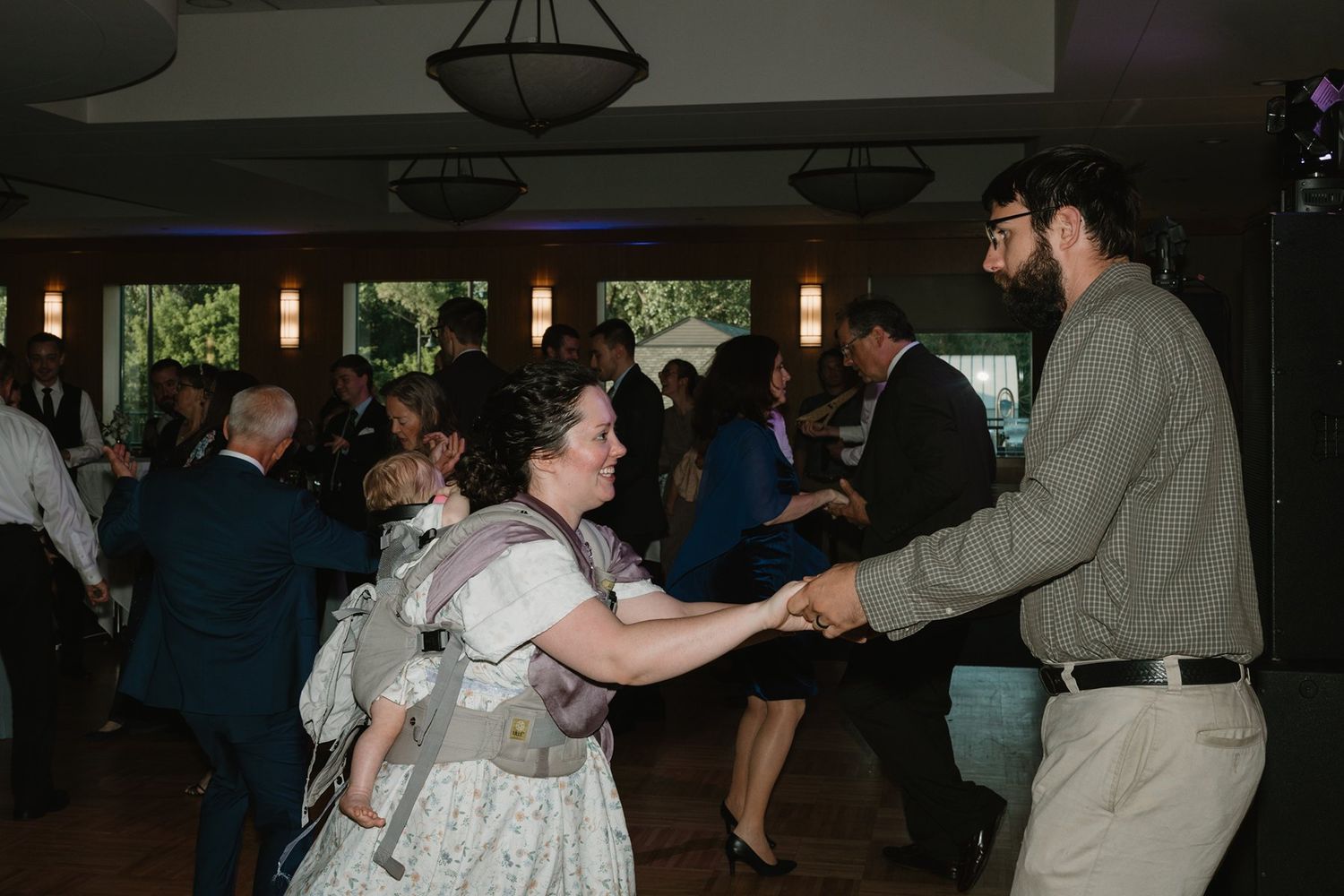 Wedding guests dancing and celebrating on a dance floor in a dimly lit reception hall.