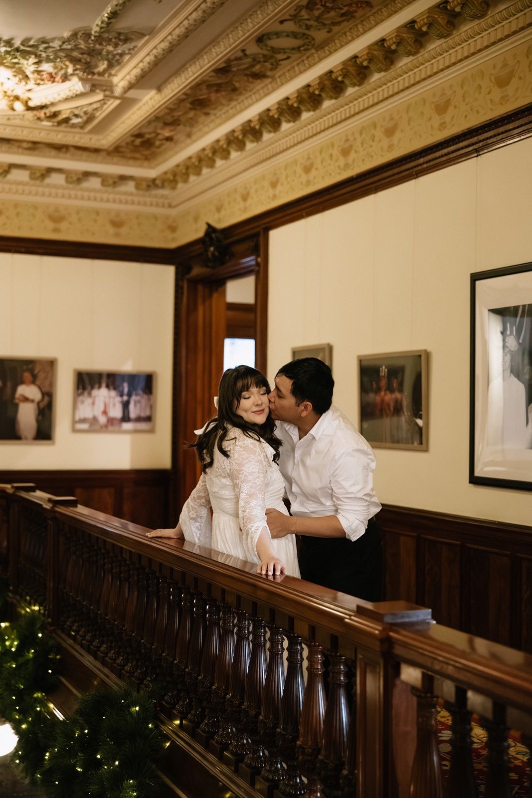 A man kisses a young girl in a white dress on a wooden staircase in an elegant historic building.