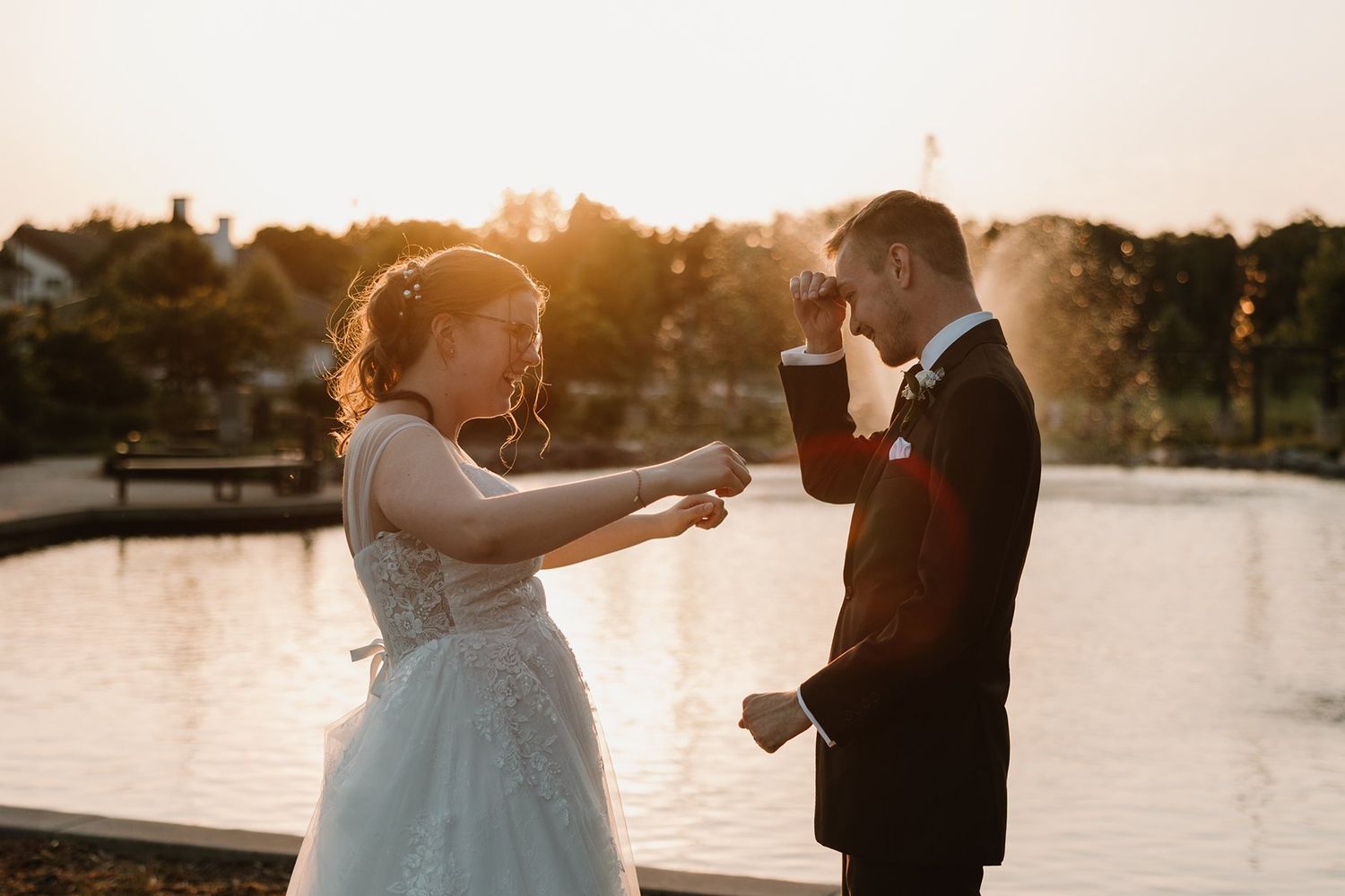 Couple shares a joyful moment during their sunset wedding photoshoot by a serene waterfront.