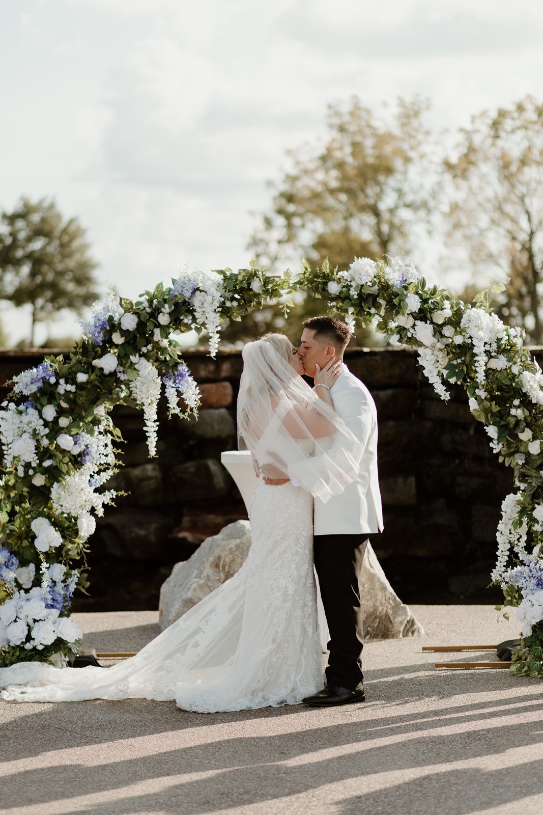 A romantic wedding ceremony moment under a white floral arch adorned with cascading blooms and greenery.