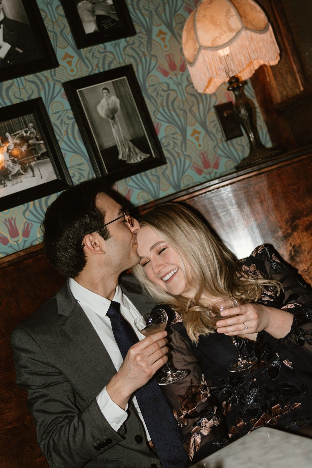 Two people share an intimate moment at a table with wine glasses and vintage decor on the walls.