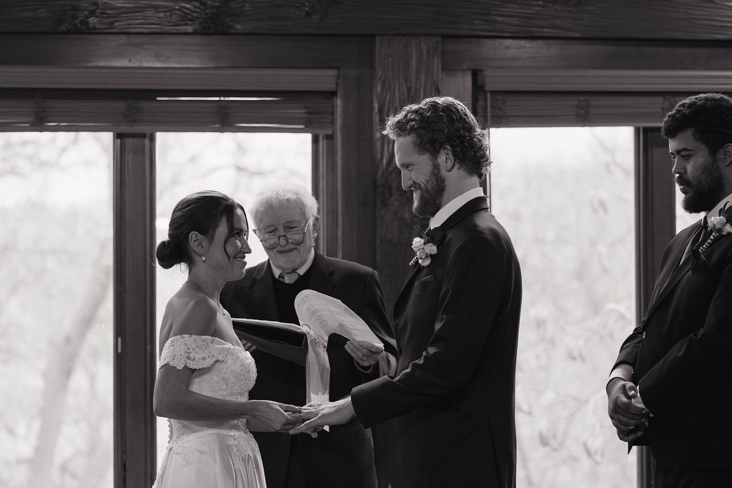 A black and white photo of a wedding ceremony with a couple holding hands in front of an officiant.