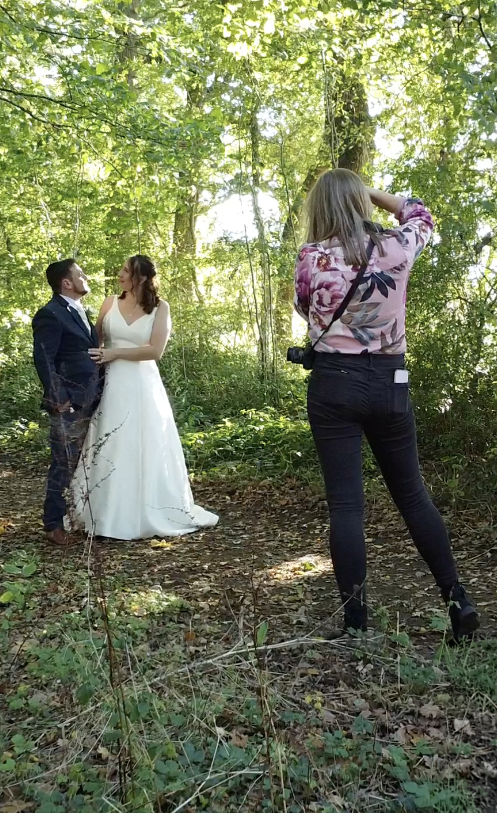 Wedding couple and photographer moving through a wooded area during photo session.