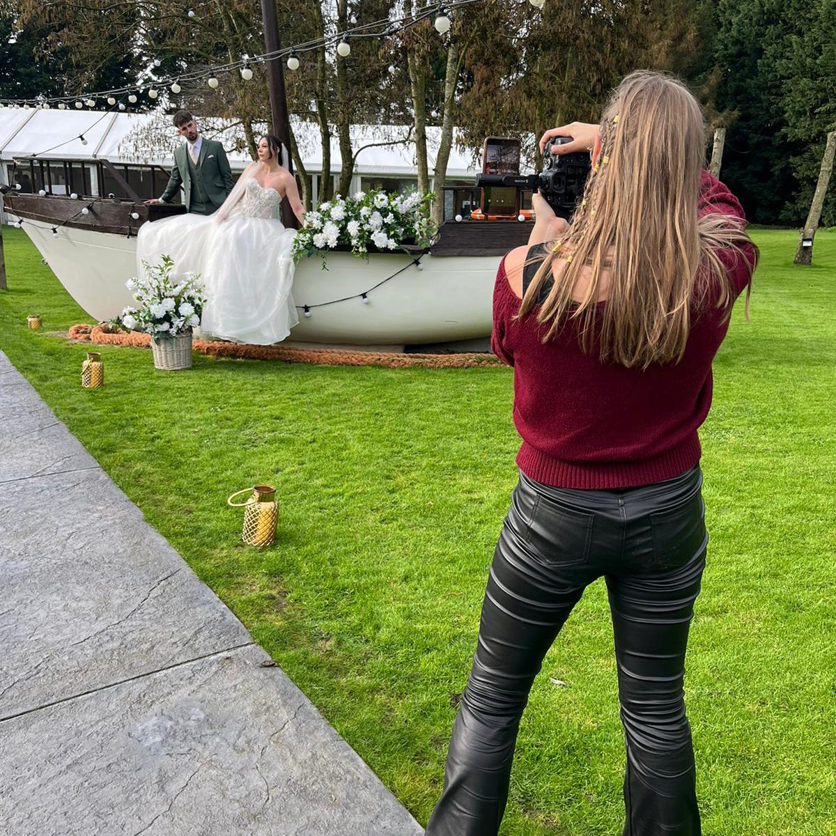 Wedding photographer in burgundy shirt taking photos on a grassy lawn.