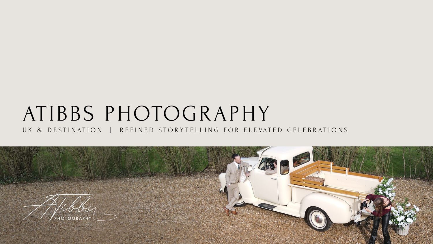A white classic car decorated with floral arrangements and ribbons parked in front of a rustic wooden building.