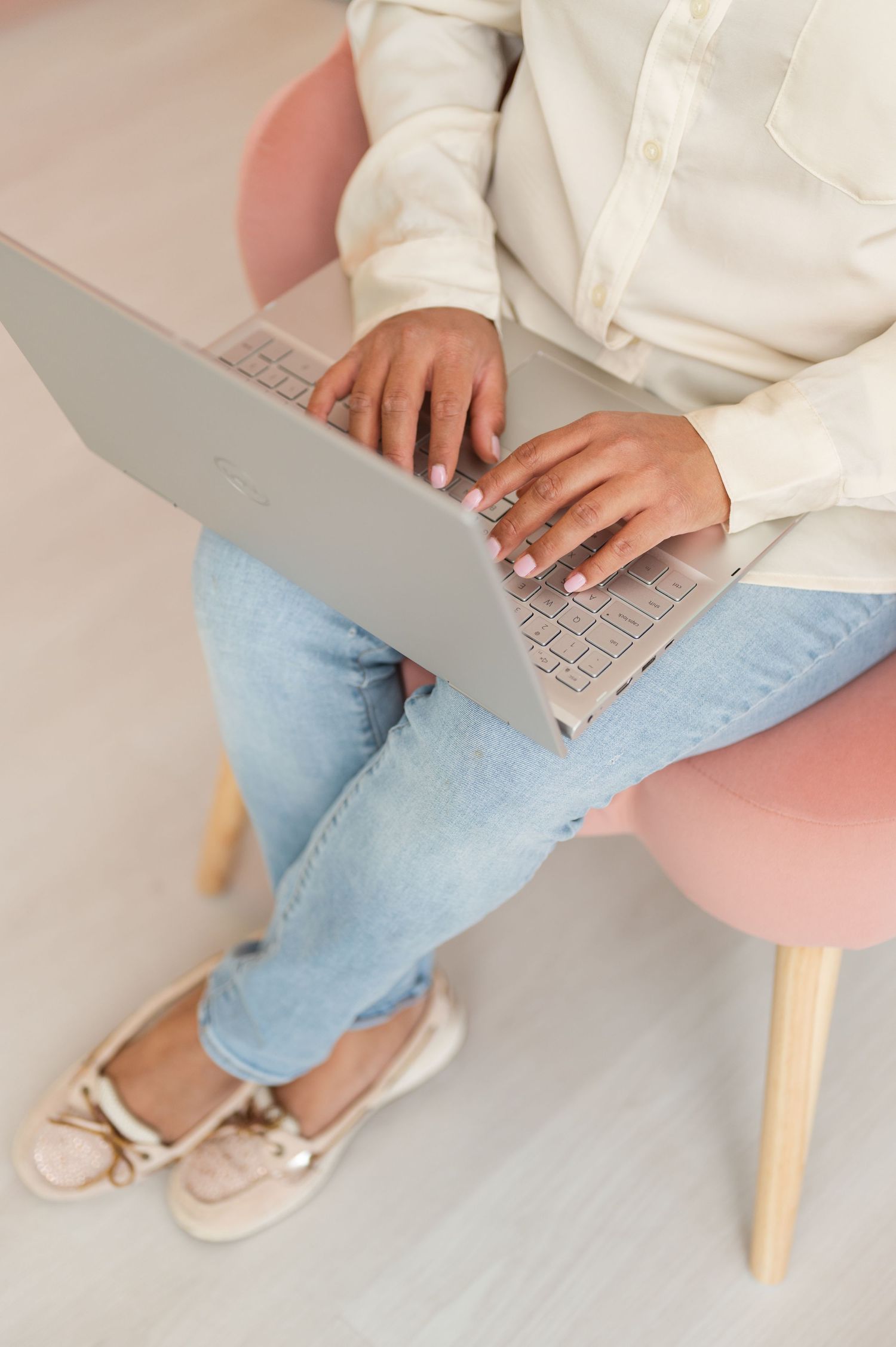 Person in casual attire working on laptop while sitting in pink chair.