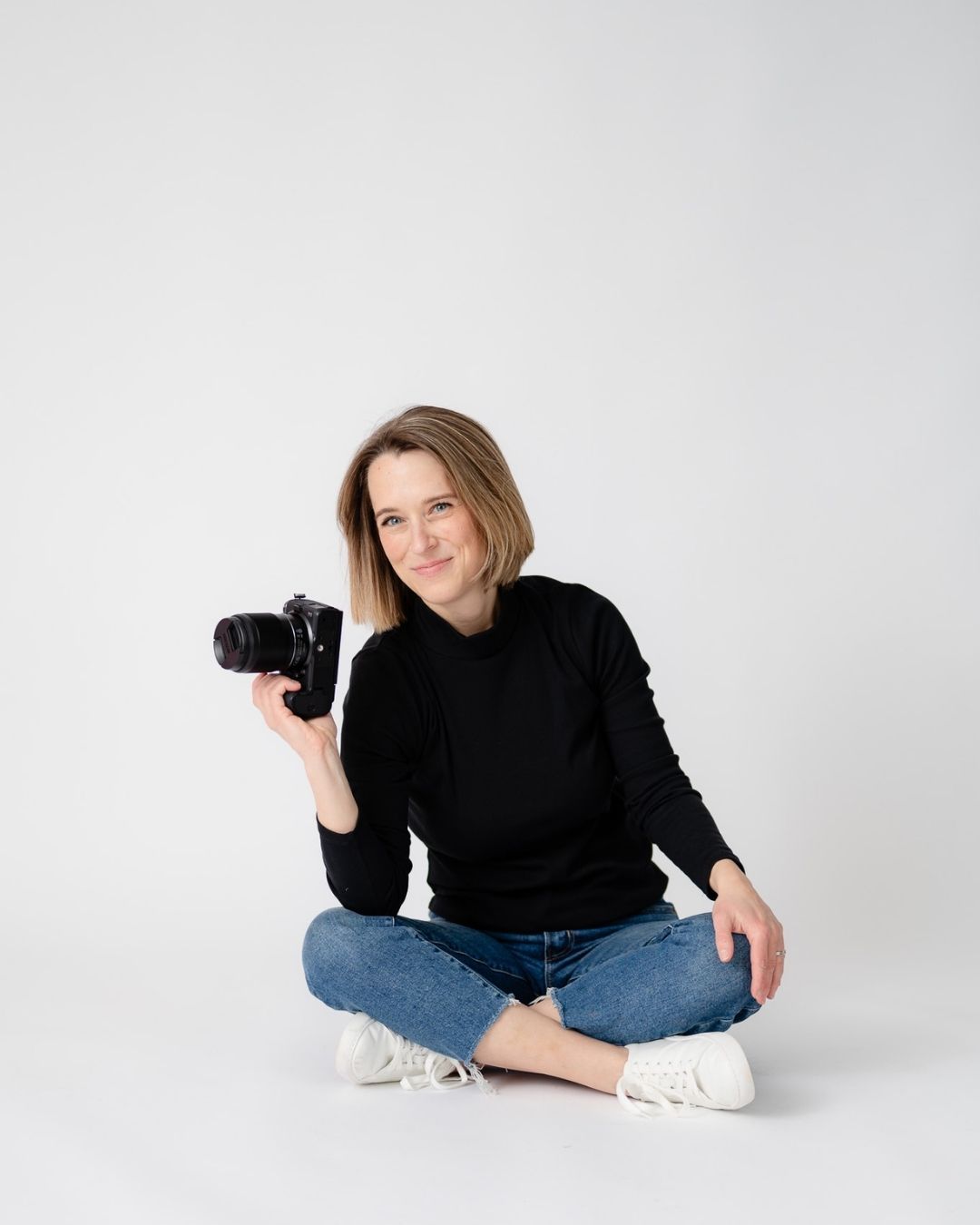 A photographer in a black sweater and jeans sits casually on a white backdrop in four different relaxed poses.