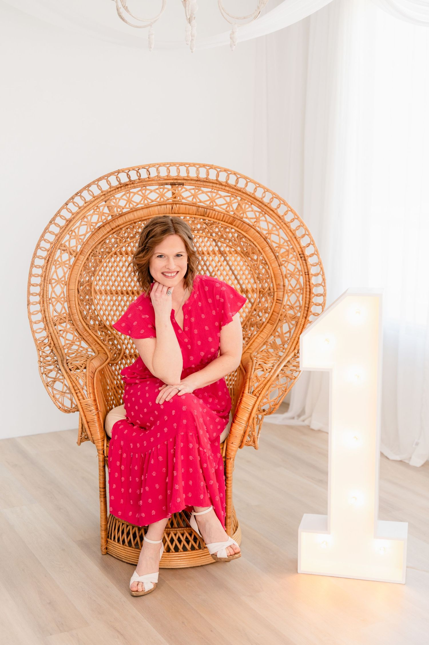 Portrait in peacock wicker chair wearing red polka dot dress with illuminated number one.