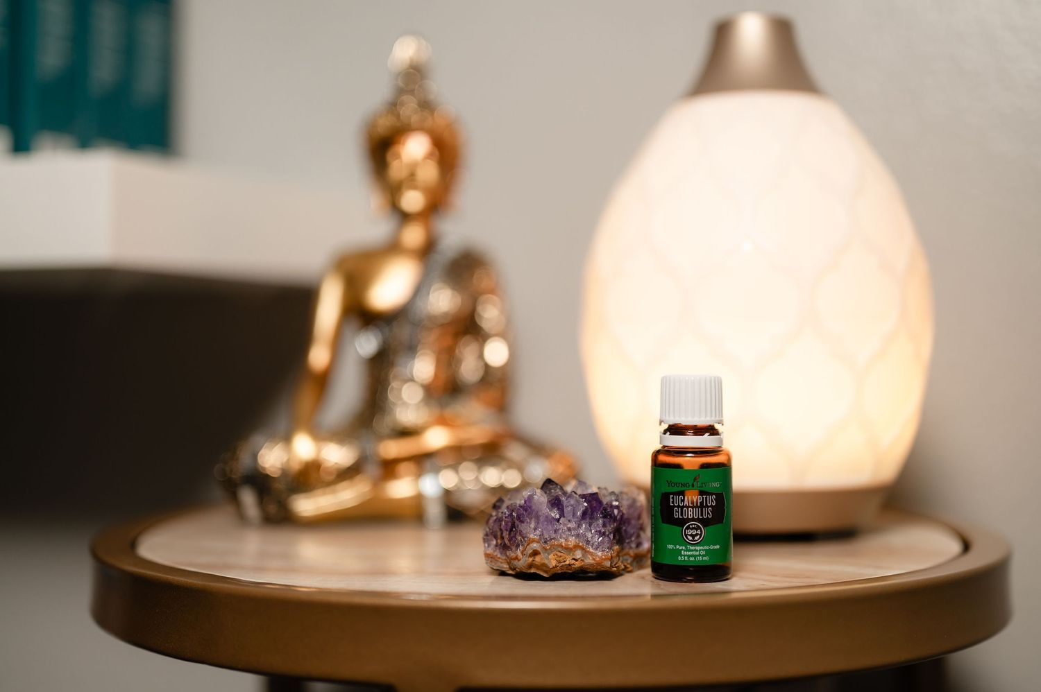 Wellness scene with essential oil bottle, crystal, and golden Buddha statue next to glowing diffuser.