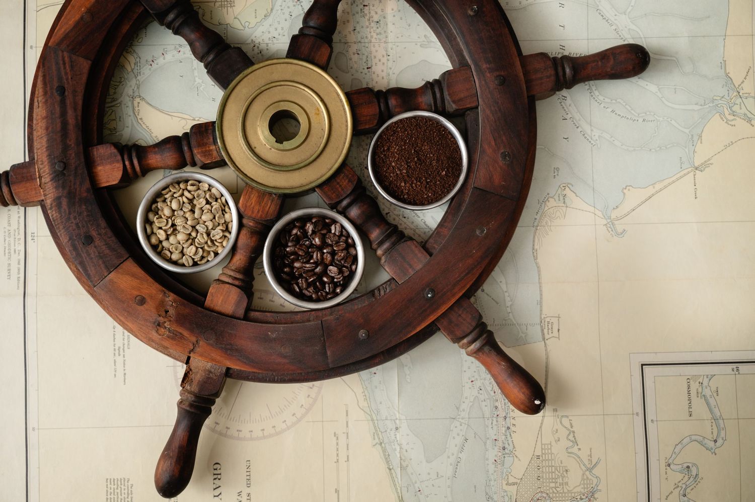 Decorative ship wheel with bowls of coffee beans and grounds displayed on map background.
