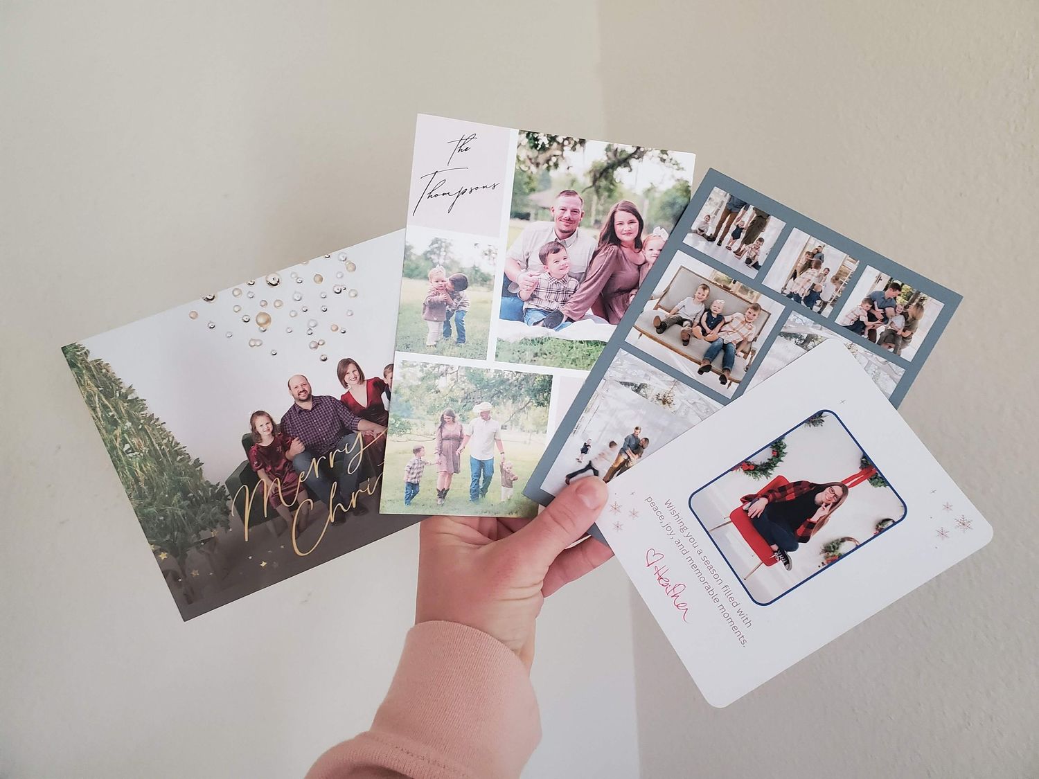 A hand holds a collection of printed photos and greeting cards spread out in a fan arrangement.