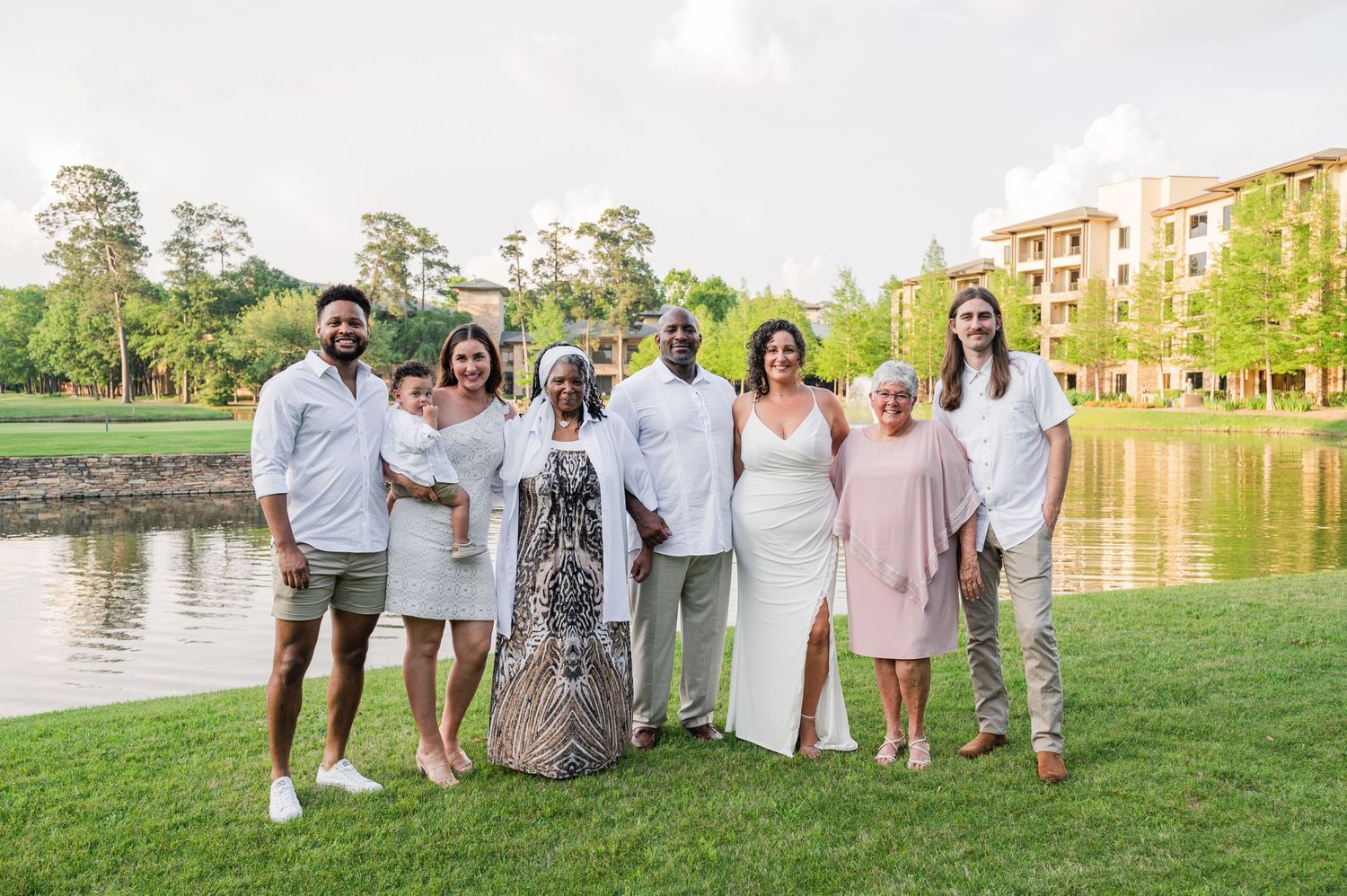 A group of people in coordinating outfits pose together by a scenic lake with apartment buildings in the background.