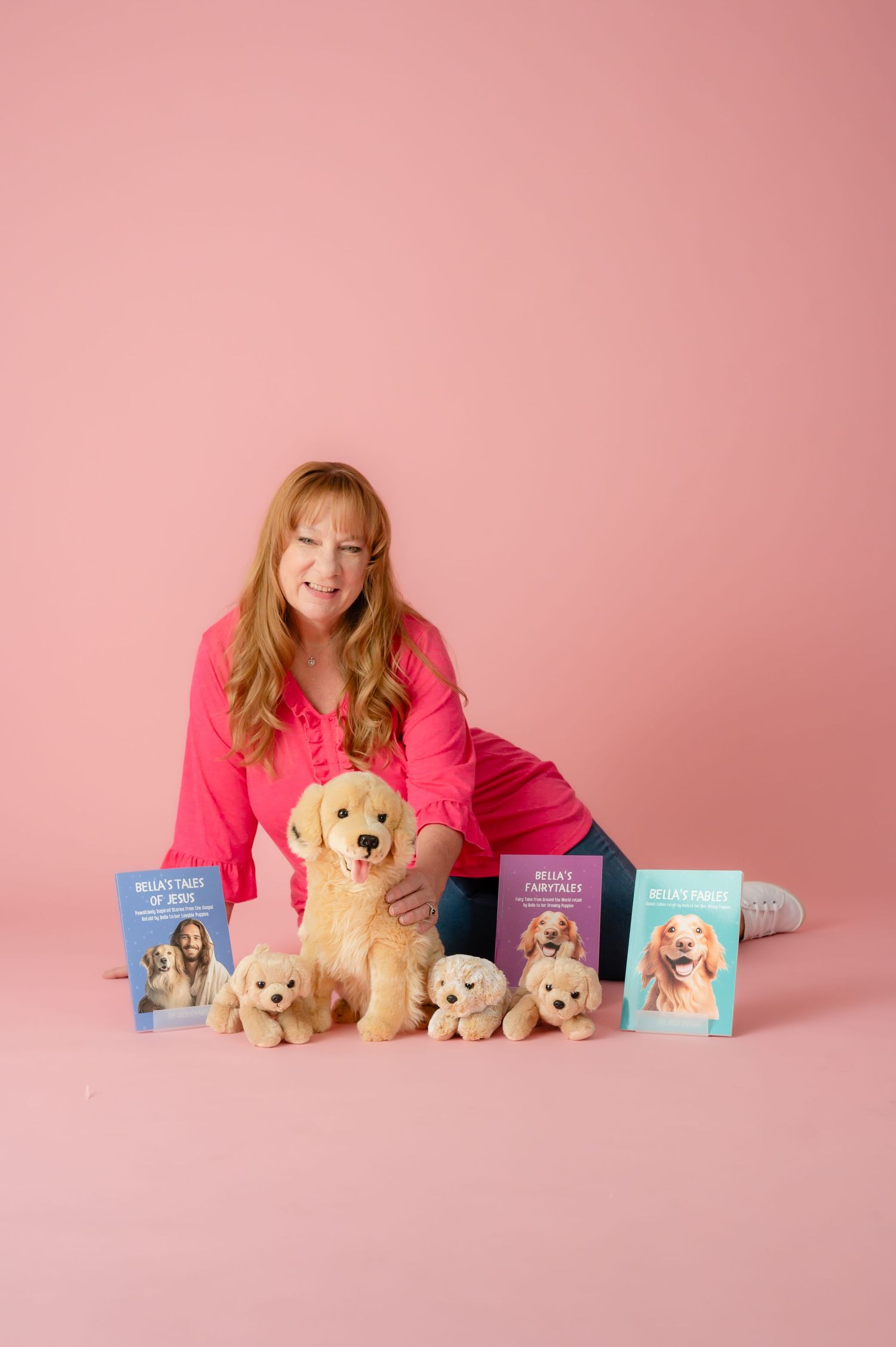 Person in pink sitting with golden retriever puppies and books on pink background.